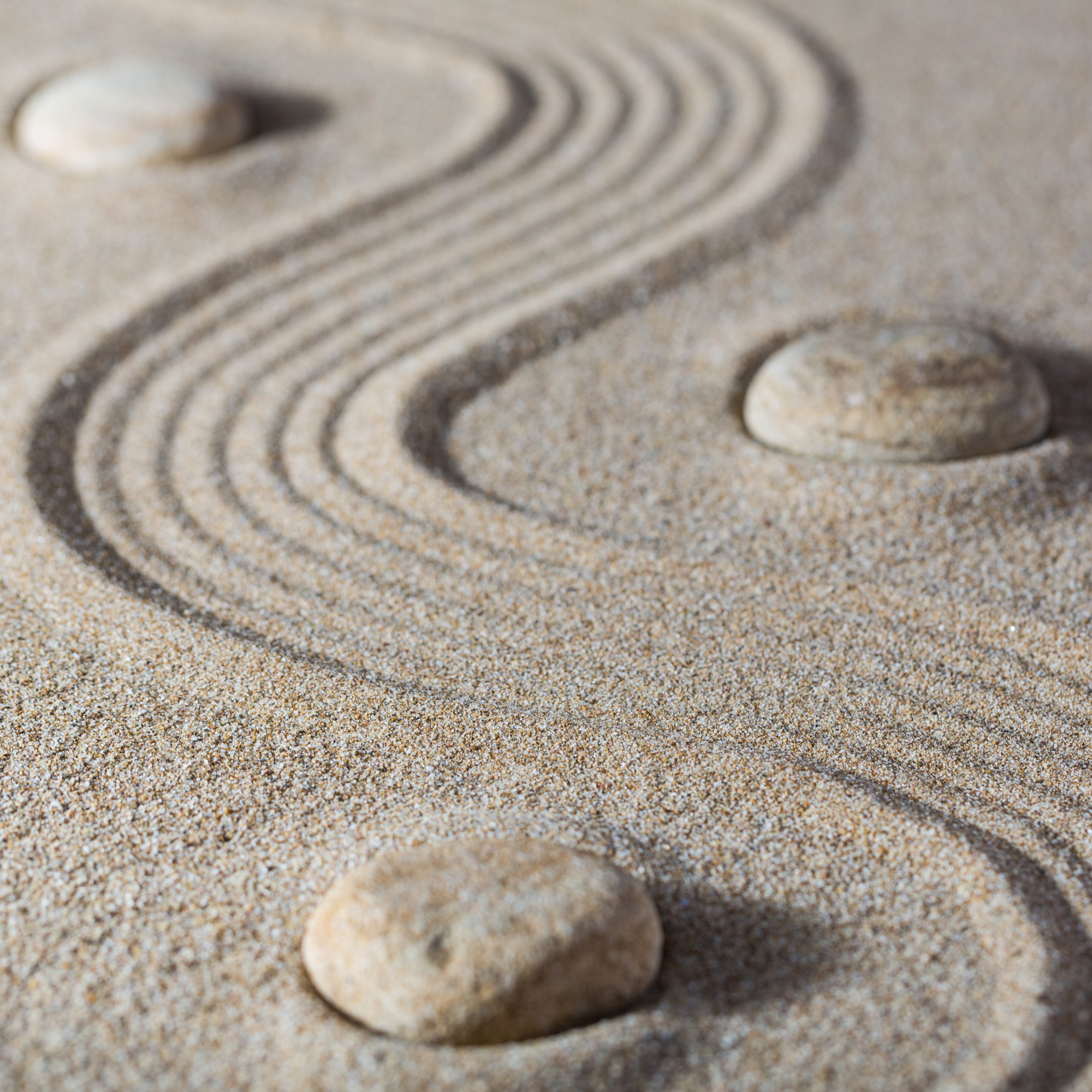 Nahaufnahme von Sand mit einer großen, flachen Stein im Vordergrund und spiralförmigen Mustern im Sand, die vom Stein oder vom Wind entstanden sind.