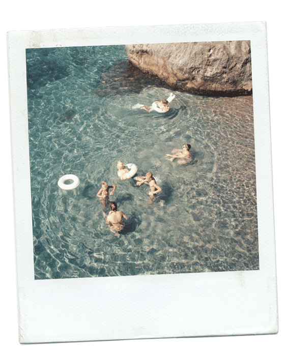 People swimming and playing in a natural freshwater pool near a large rock.