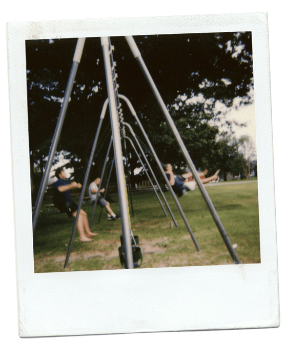 Children swinging on a playground set in a park with trees in the background