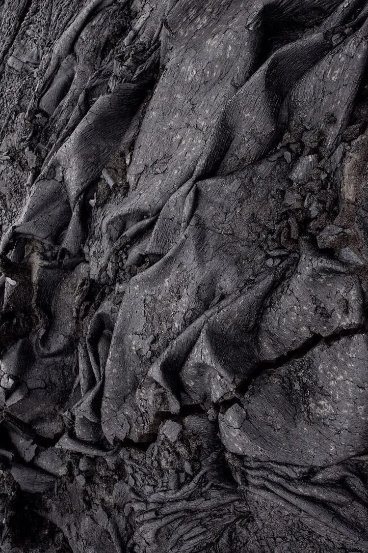 Close-up of charred, blackened wood and debris, indicating a recent fire or burning event.