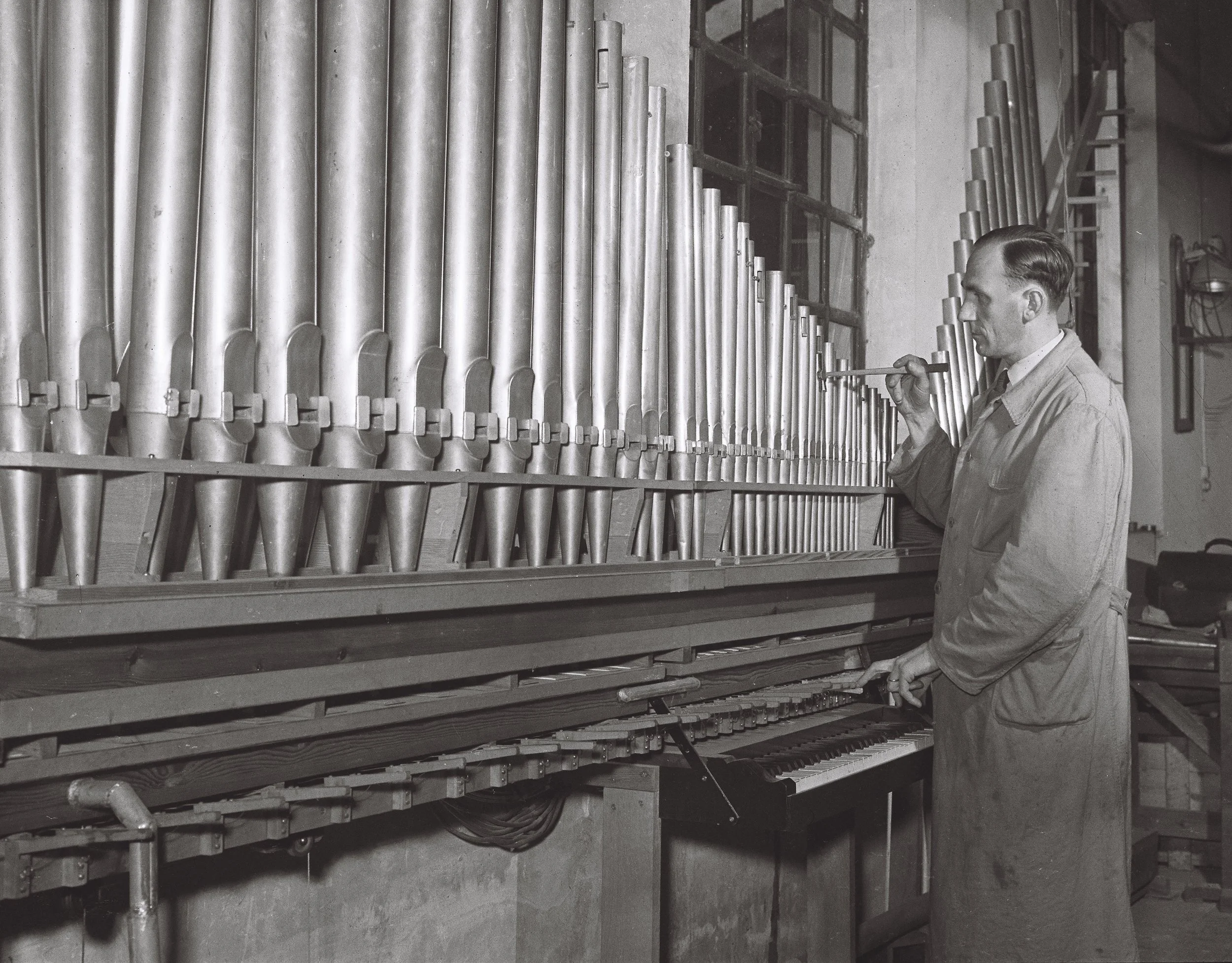 Un homme joue de l'orgue dans un atelier avec de nombreux tuyaux d'orgue en acier.