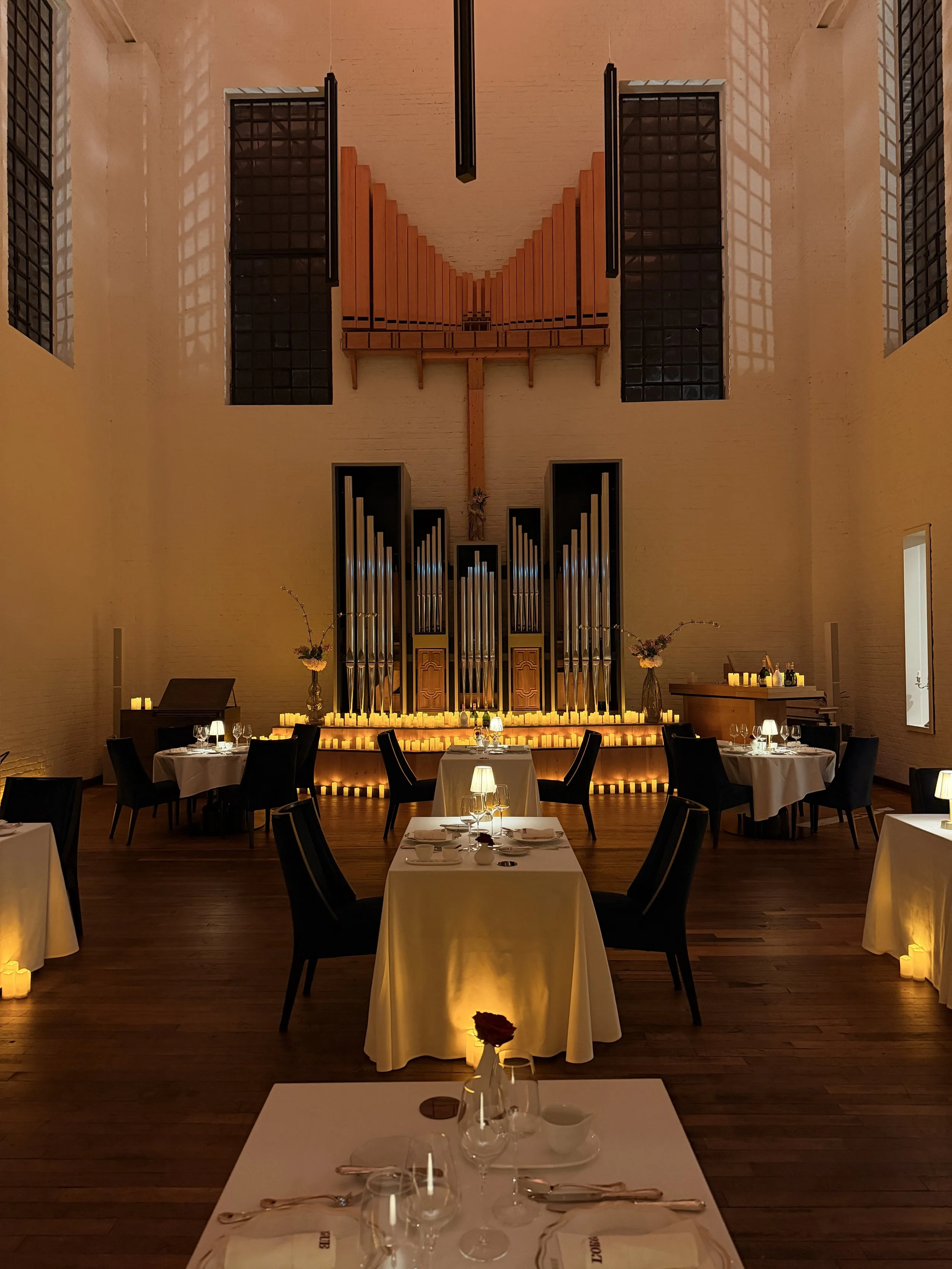 Salle de réception élégante avec des tables drapées de blanc, des bougies et une vue sur un orgue d'église, ambiance chaleureuse et sophistiquée.