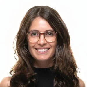 A woman with long brown hair, wearing glasses and a black top, smiling at the camera.