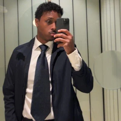 Young man in a suit taking a mirror selfie in a bathroom or fitting room.
