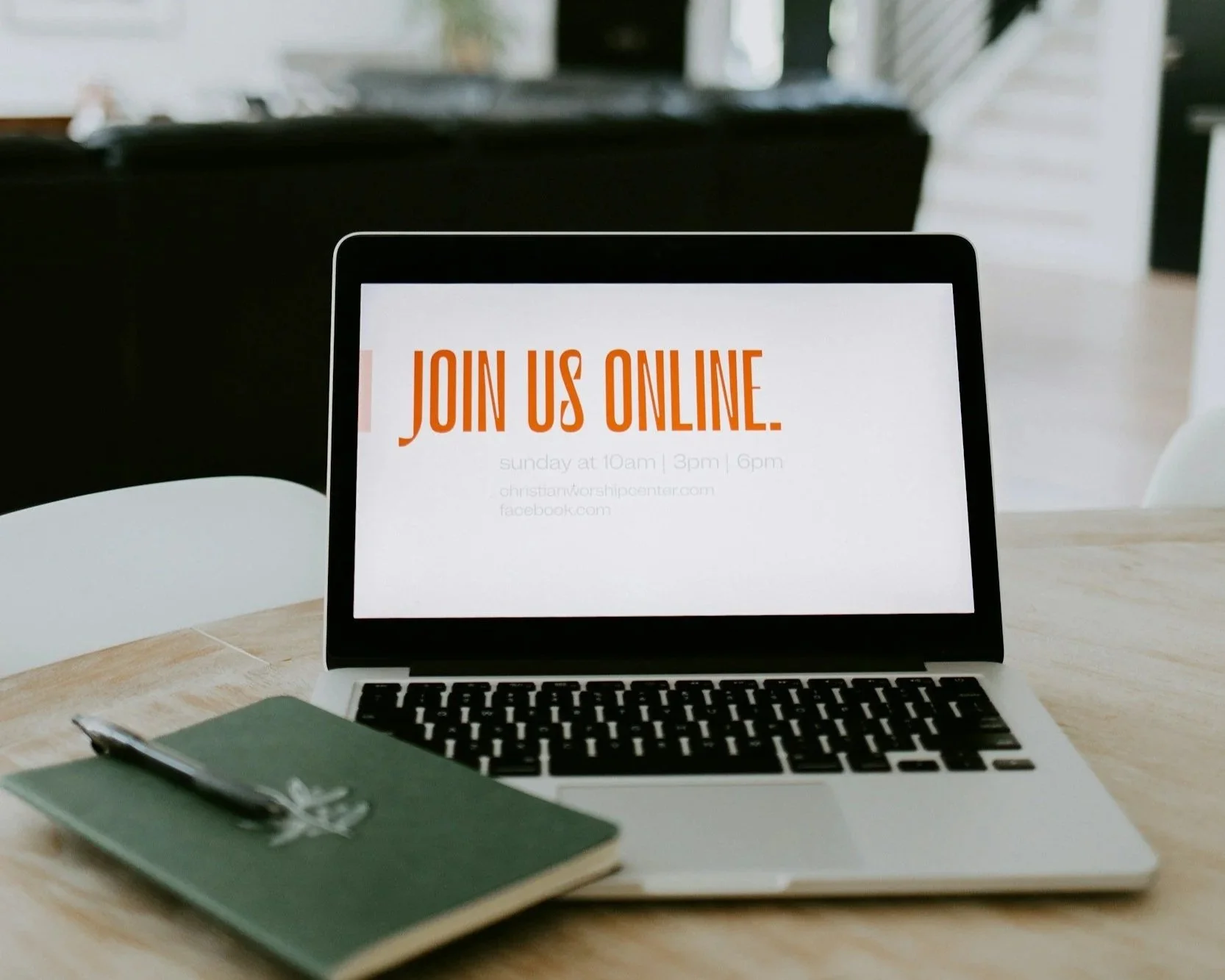 Laptop displaying a message to join an online event, placed on a light wood table with a green notebook and a pen in the foreground.