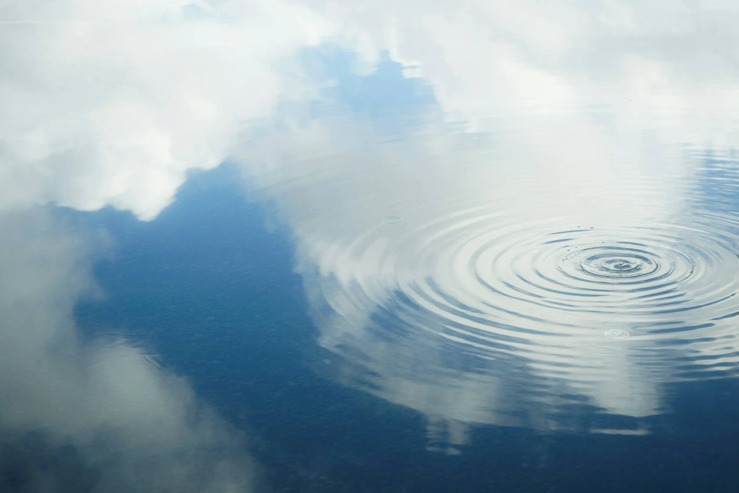 Sky with clouds reflected on calm water, with ripples near the bottom right.