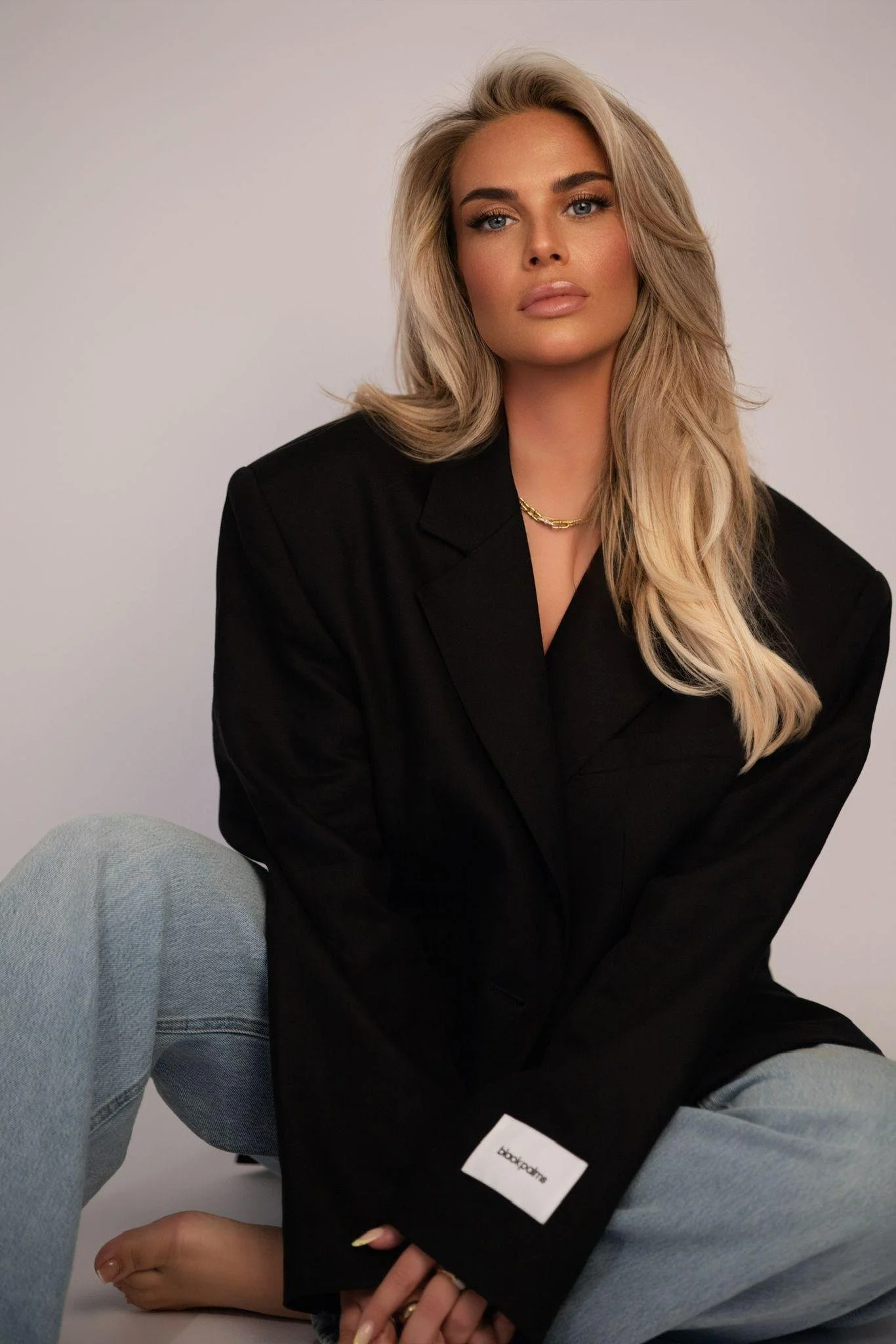 Junge Frau mit langen blonden Haaren und natürlichem Make-up vor neutralem Hintergrund