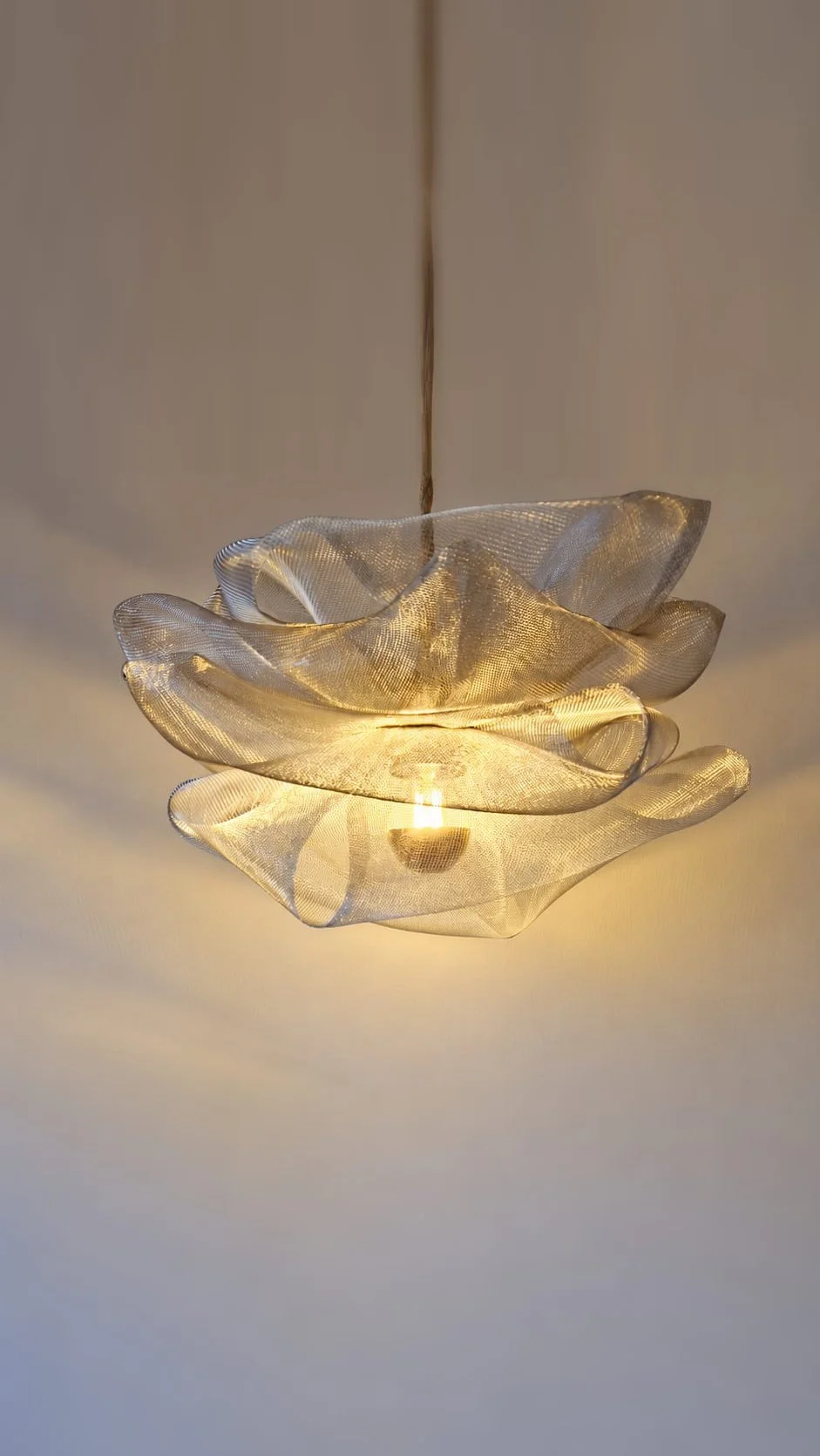 Lampe design artisanale en métal brut argenté avec ampoule à lumière jaune. Modèle Lully en suspension, studio Cajoa.