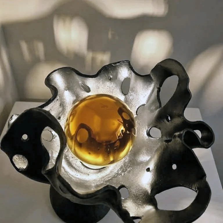 Une sculpture lumineuse contemporaine en argile, représentant une forme organique avec des trous, contenant une ampoule à calotte dorée centrale qui reflète la lumière.