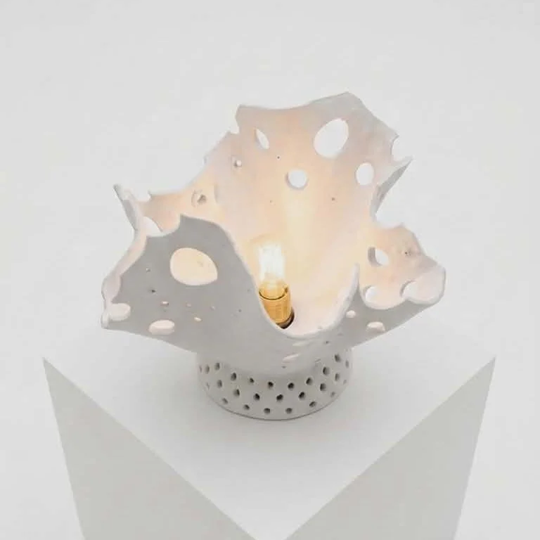 Une sculpture lumineuse d'argile en forme organique de fleur avec des trous pour laisser se projeter la lumière.