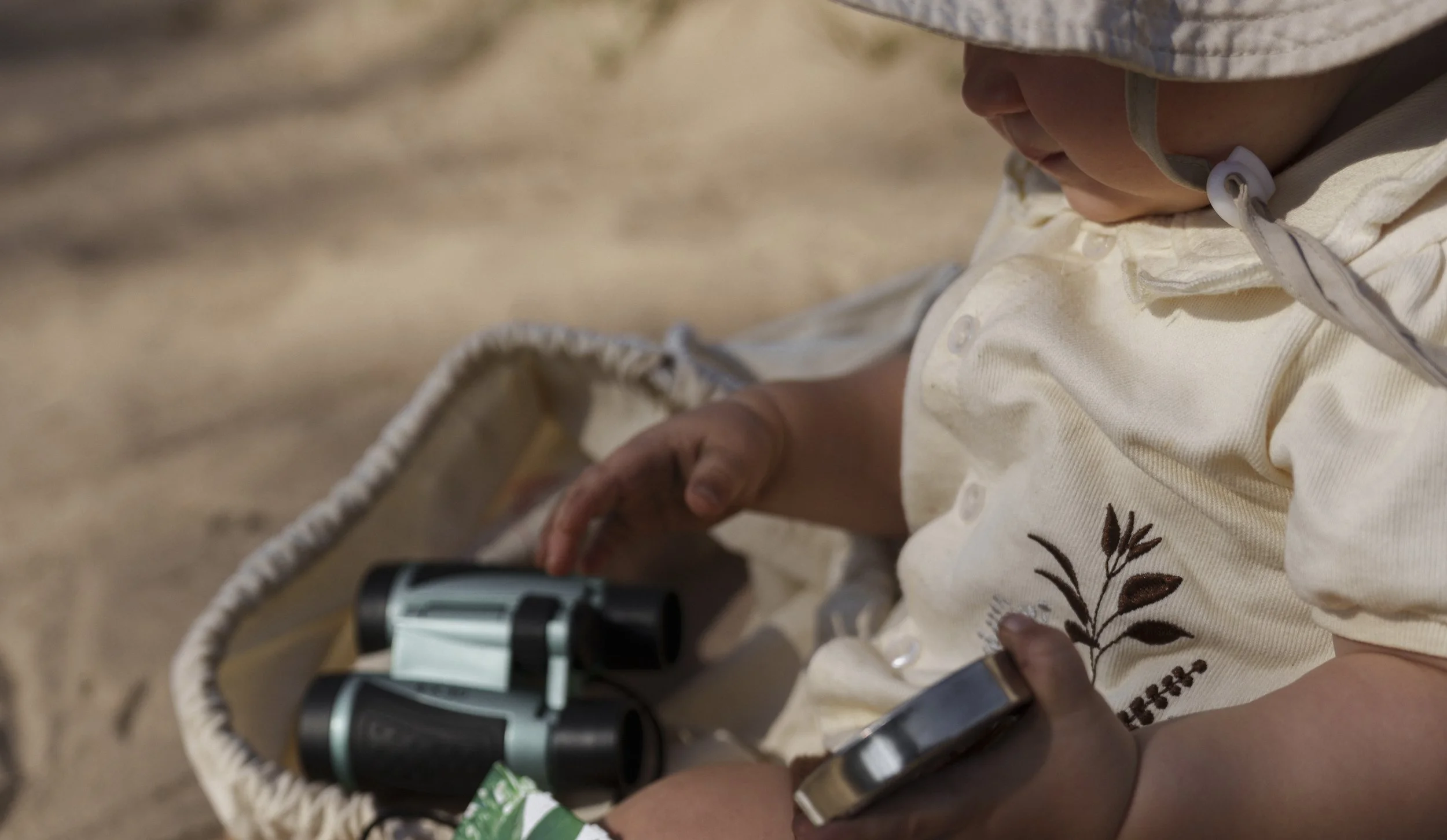 Toddler exploring a safari welcome pack with binoculars, hat and canvas bag