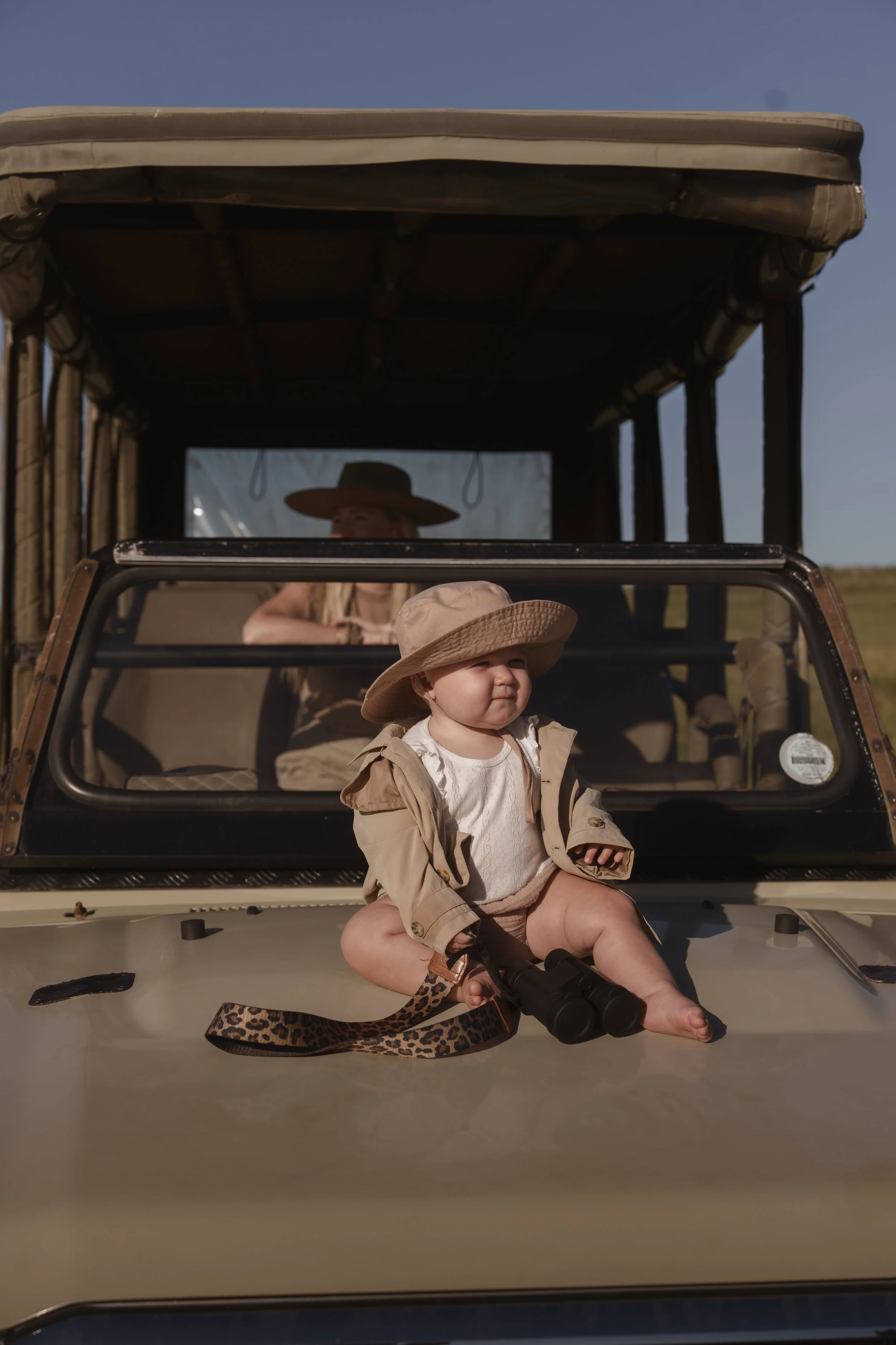 Baby in a sun hat sitting on the bonnet of a safari vehicle