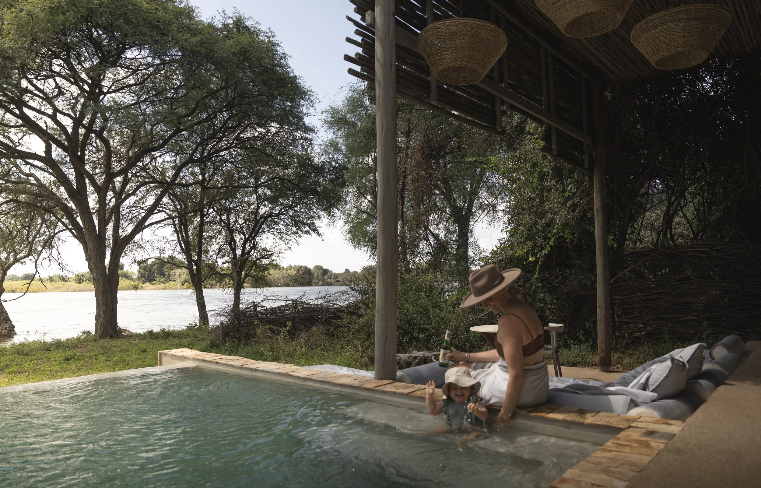 Toddler sitting at the edge of an unfenced plunge pool with a parent close by