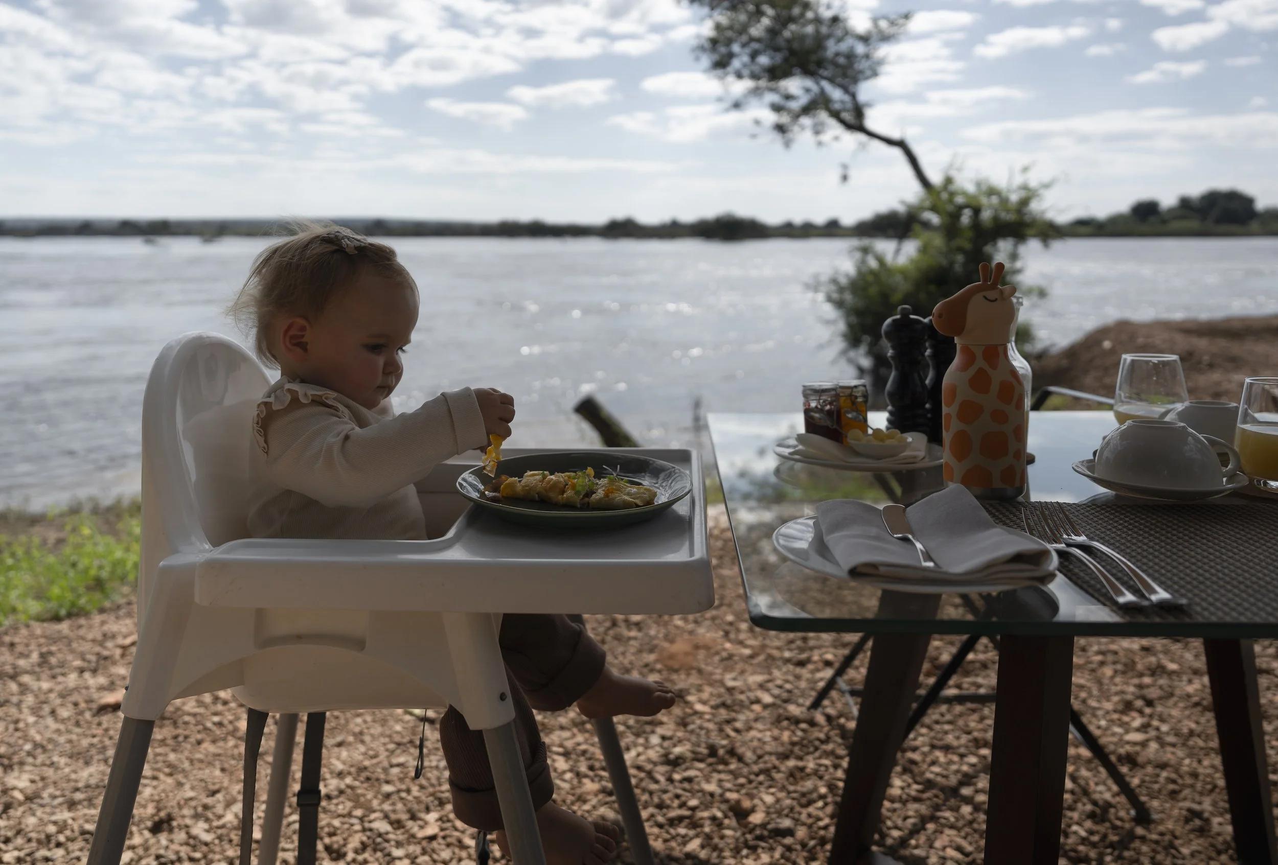 Toddler eating breakfast in a high chair on a lodge deck overlooking a river