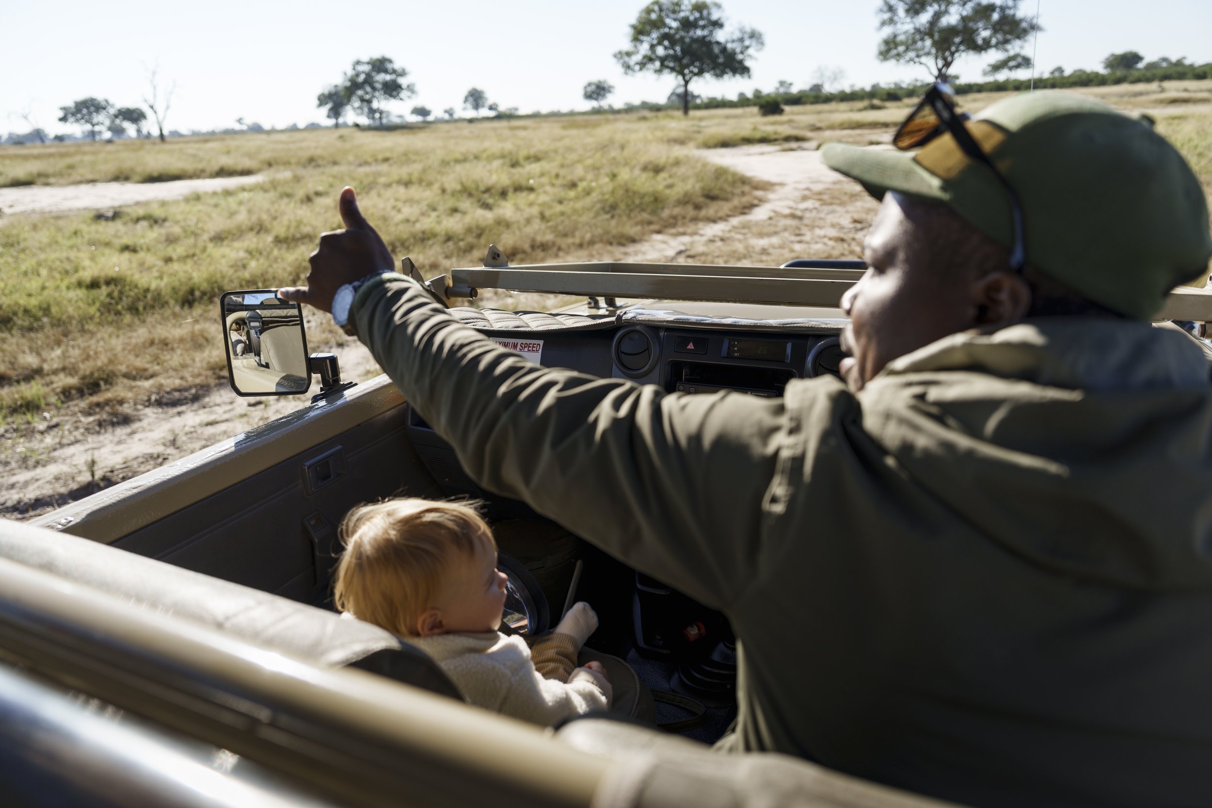 Safari guide pointing out wildlife to a toddler seated alone in a private safari vehicle