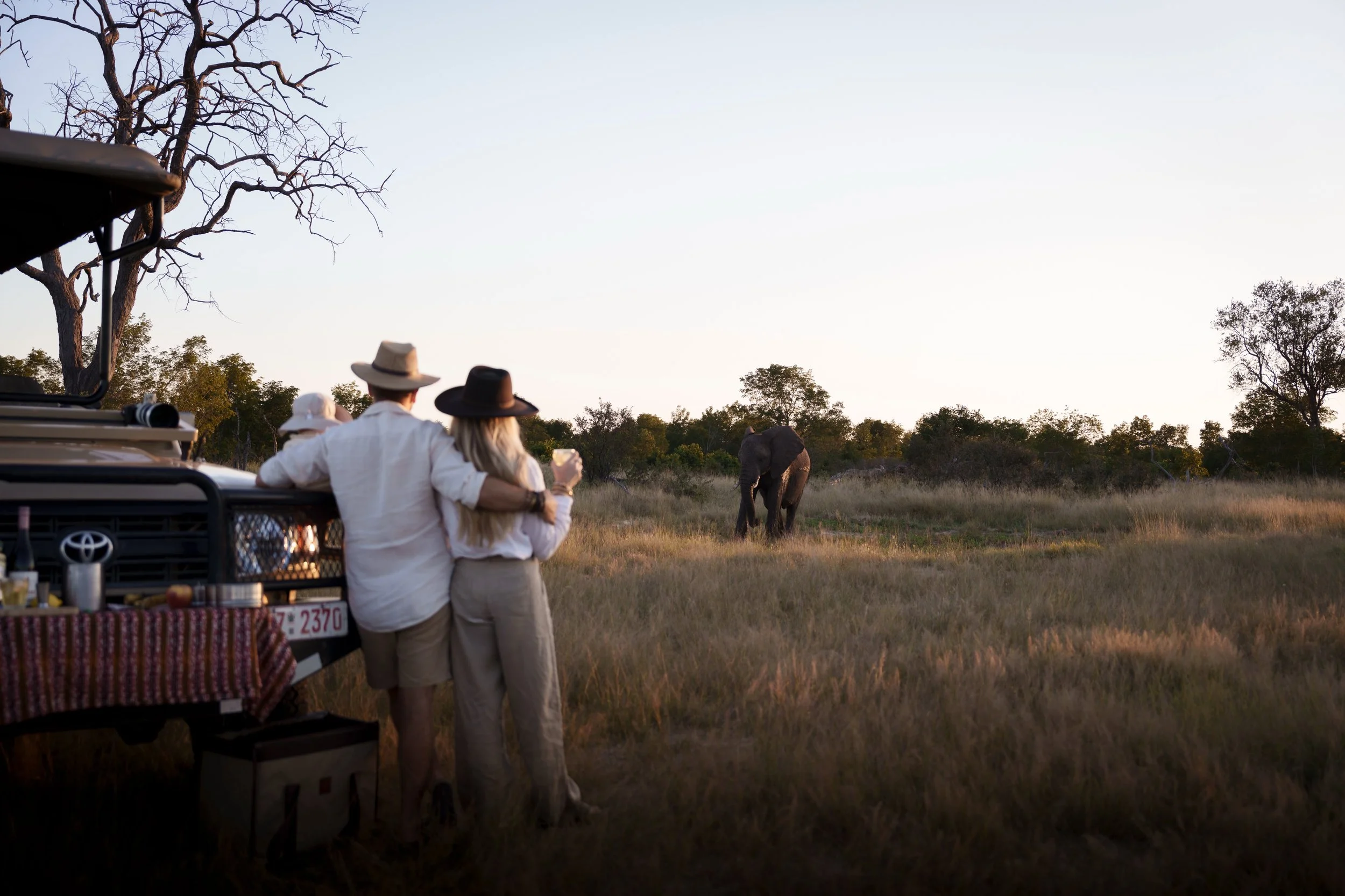 Parents and their child watching an elephant from beside a safari vehicle at a sundowner stop