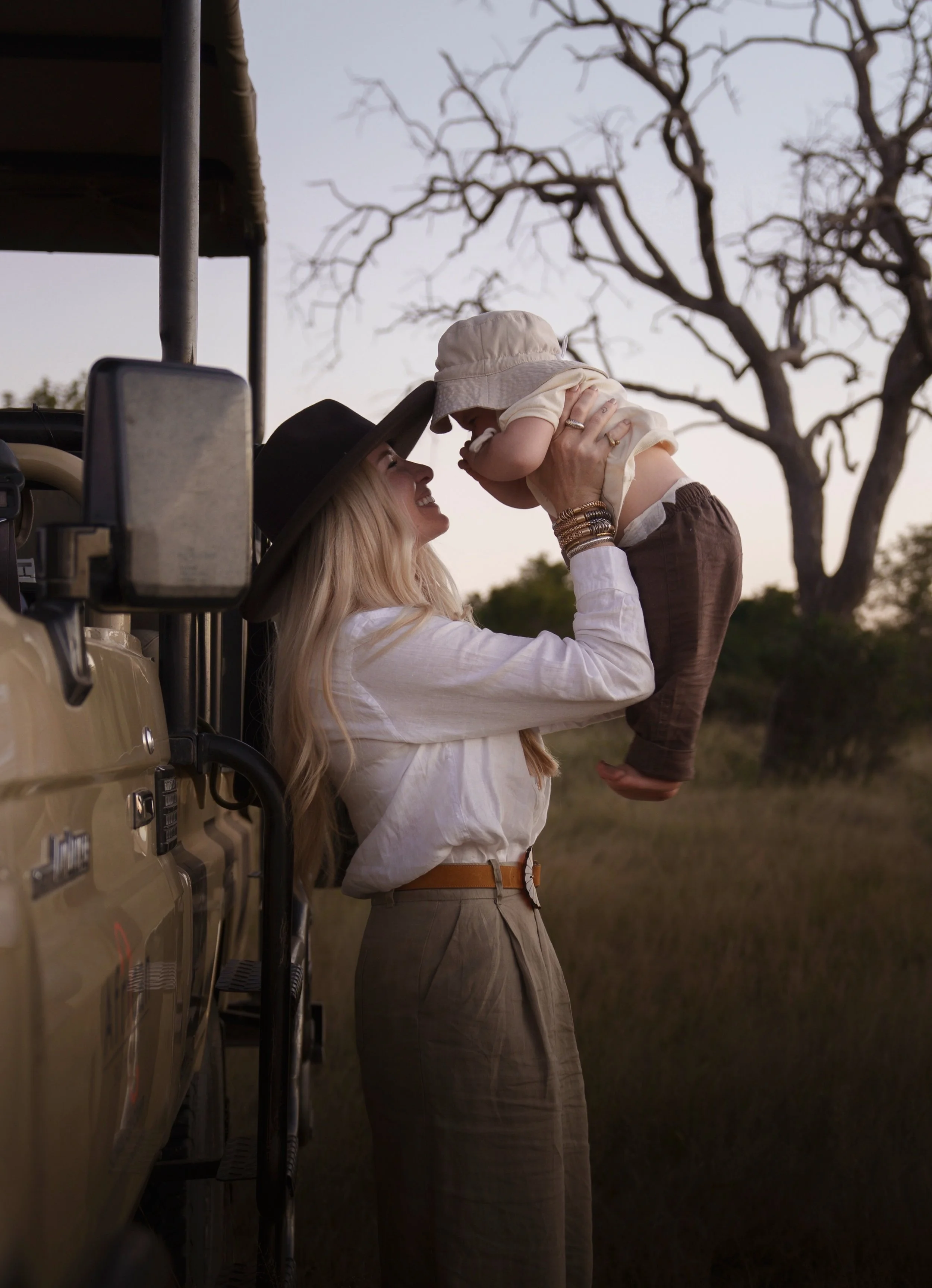 Jemma Park lifting her young daughter beside a private safari vehicle at sunset in the African bush