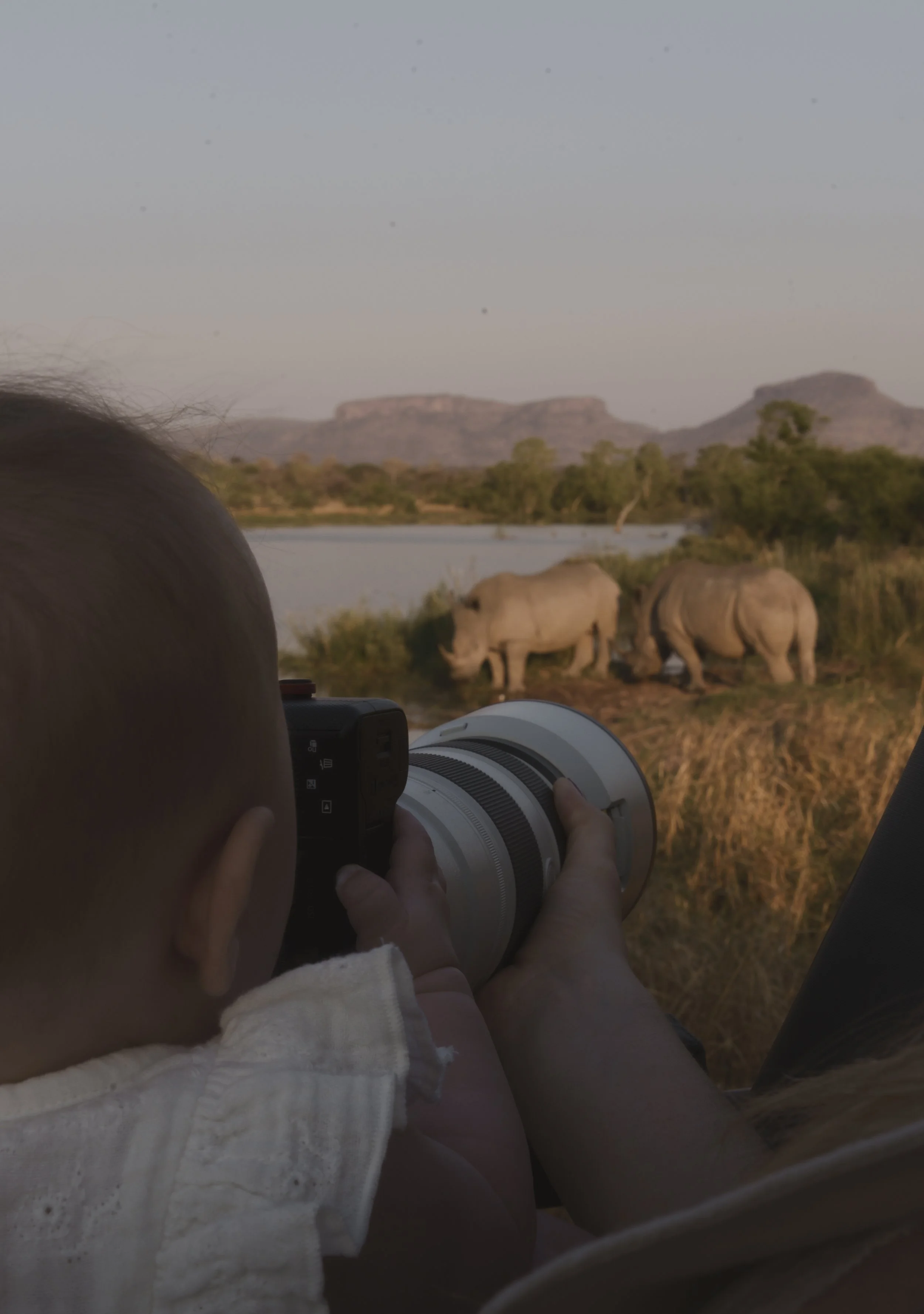 Baby holding a camera with a long lens while watching rhino from a safari vehicle
