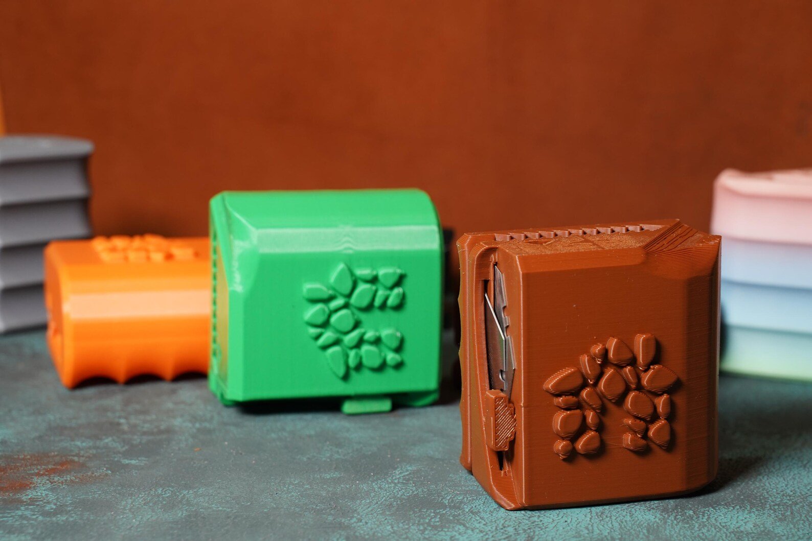 Colorful plastic clay models of a book, a flower, and a wallet arranged on a textured surface with stacked plates in the background.