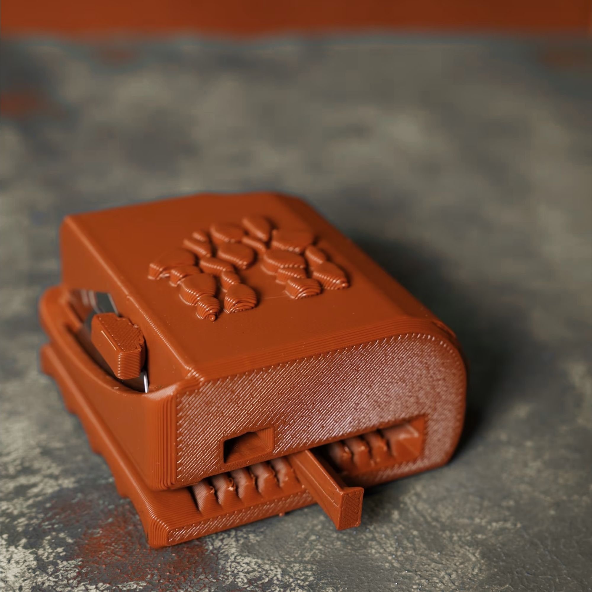 A close-up view of a miniature orange plastic bench with an intricate design on the seat, placed on a rough, textured surface.