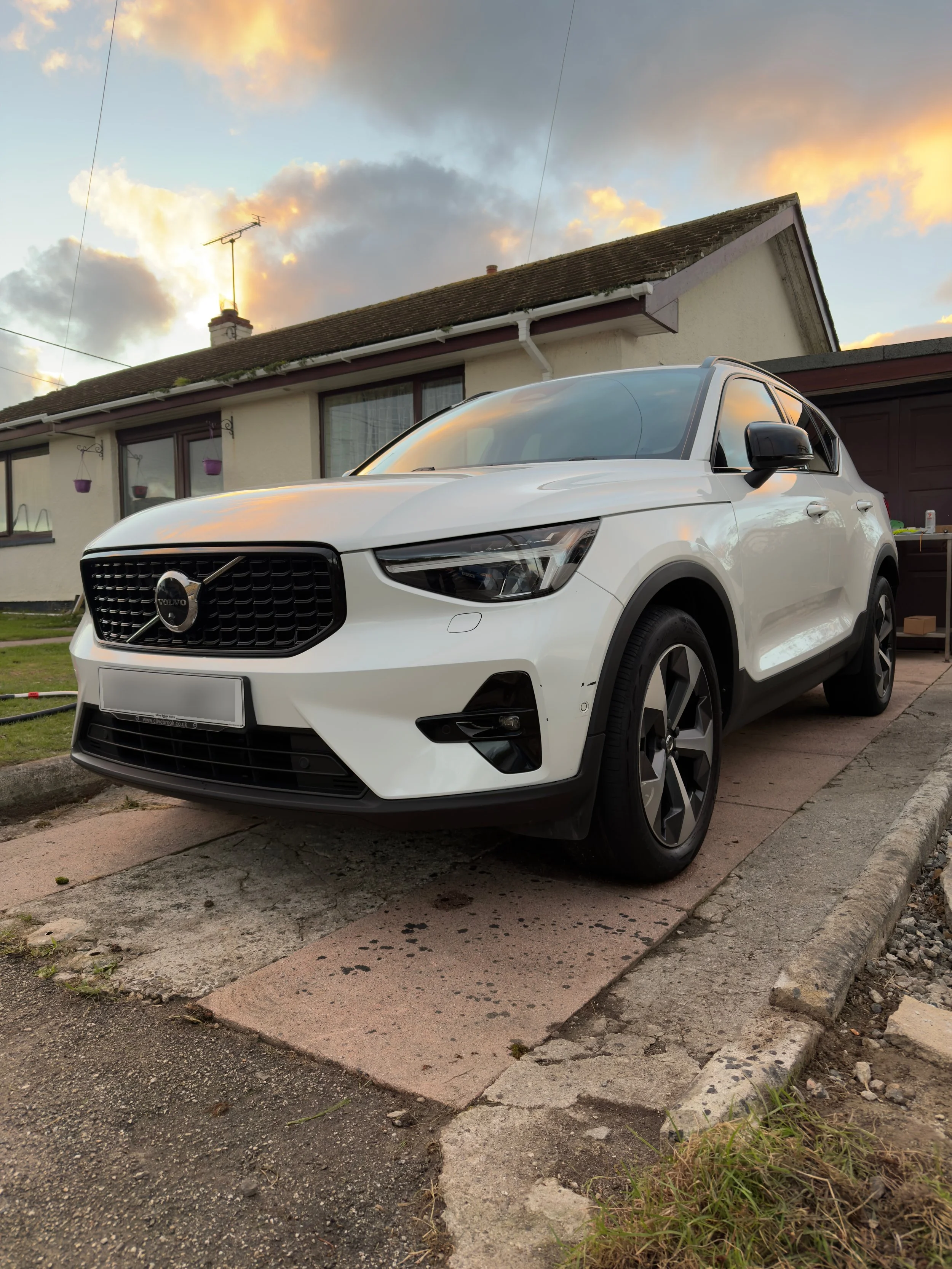 White Volvo SUV parked on a driveway in front of a house at sunset
