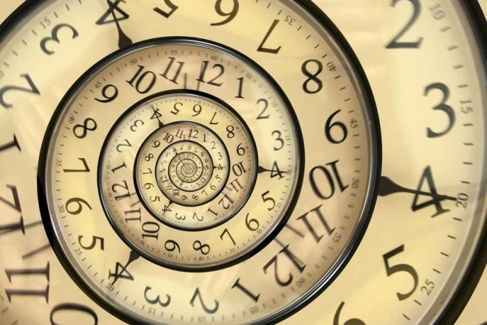 A close-up photo of a clock showing a spiral pattern of nested, infinitely repeating clock faces.