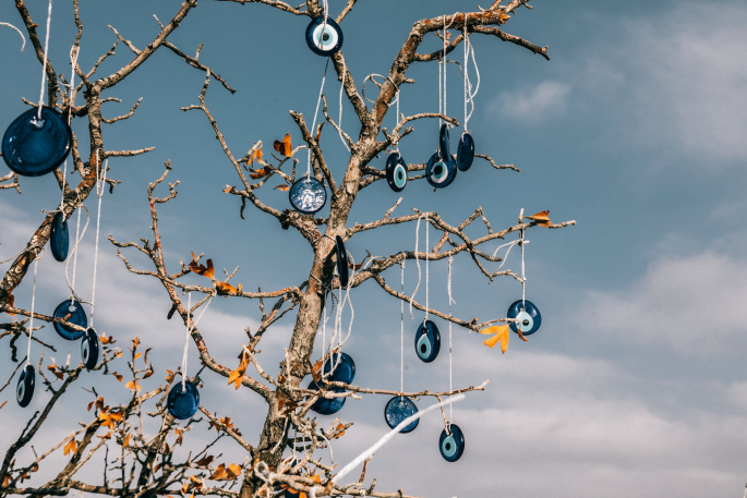Bare tree with scattered orange leaves, decorated with blue and white circular ornaments hanging from strings, against a cloudy sky.