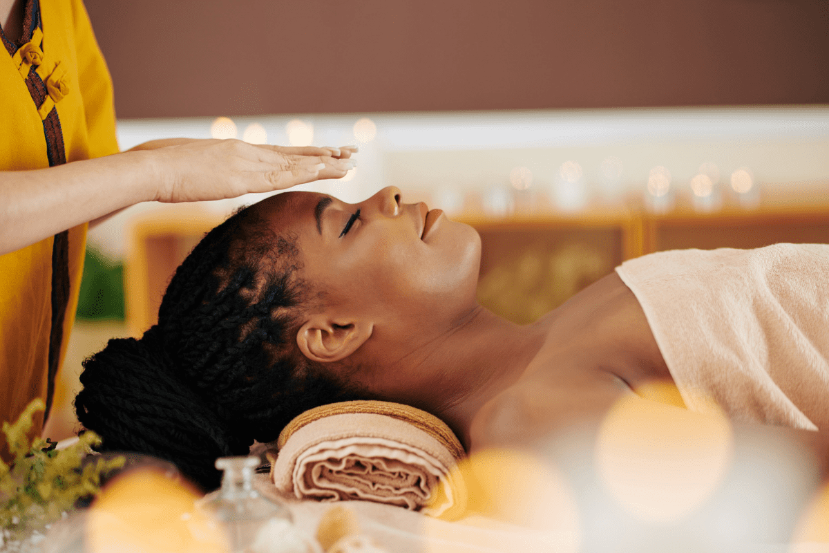 Woman receiving a forehead massage in a spa setting with candles and flowers in the background.