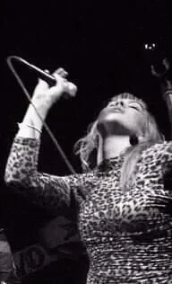 A woman singing into a microphone on stage, likely during a performance, with her head tilted back and eyes closed.