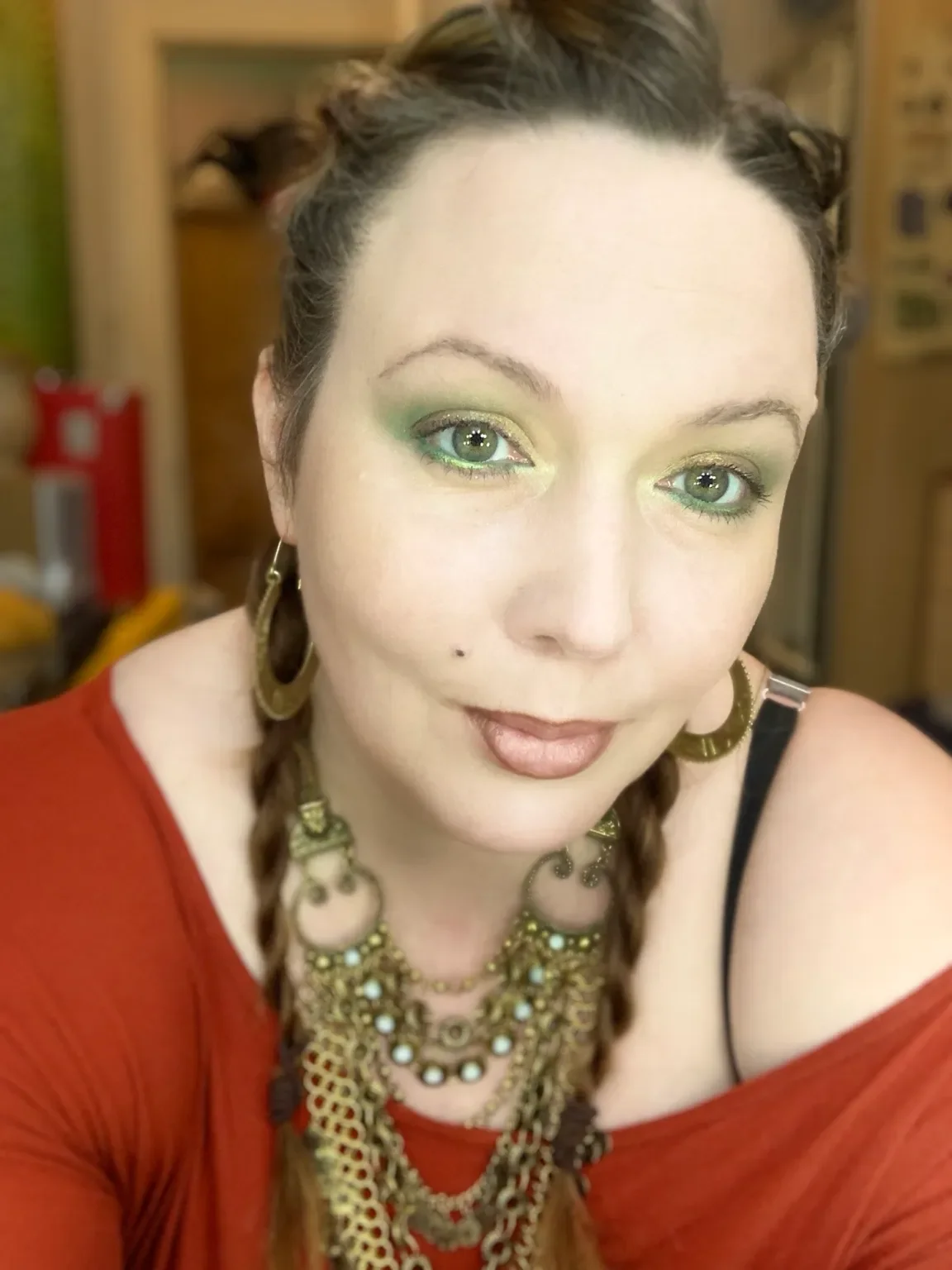 Close-up of a woman with braided hair, wearing jewelry and makeup, in an indoor setting.