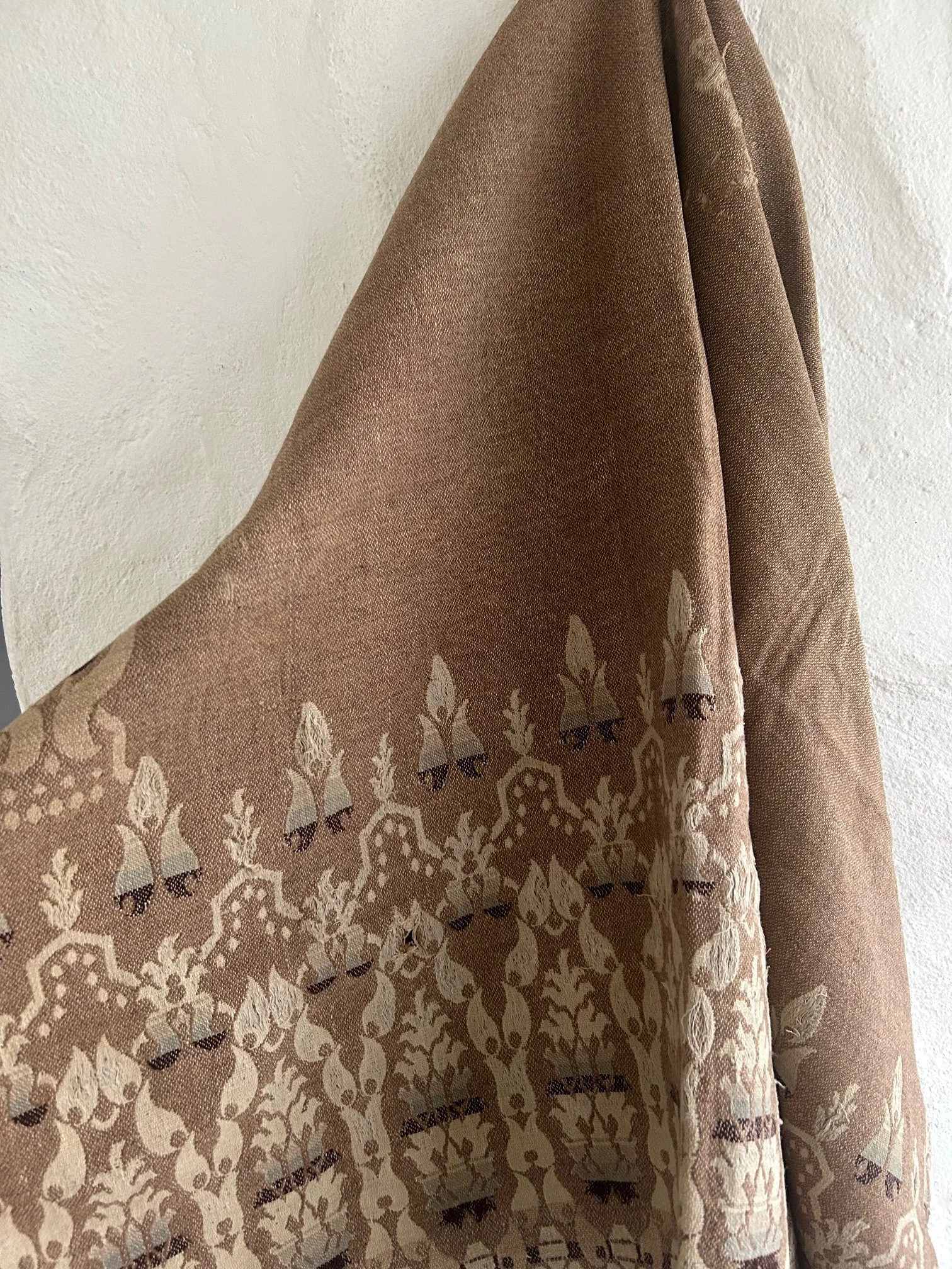 A brown fabric curtain with a decorative white pattern hanging against a white wall.