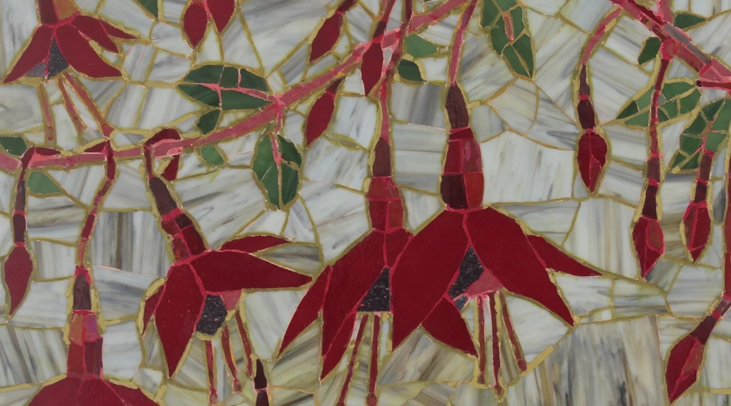 Close-up of a stained glass art piece featuring red and dark red fuschia flowers with green leaves, outlined in gold, on a light, striped background.