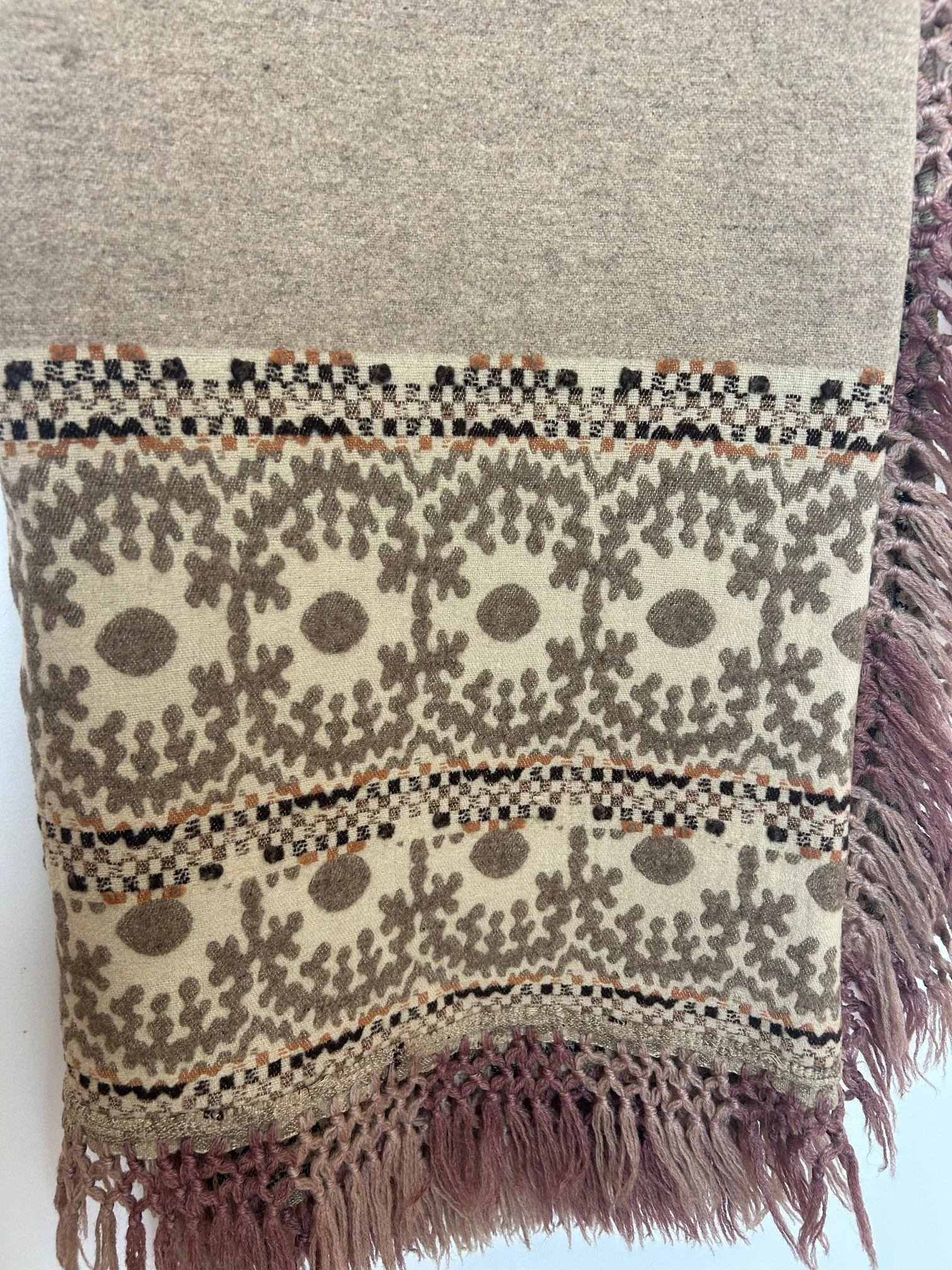 A close-up of a Shawl with intricate patterns, fringed edges, and a beige, brown, and cream color scheme.