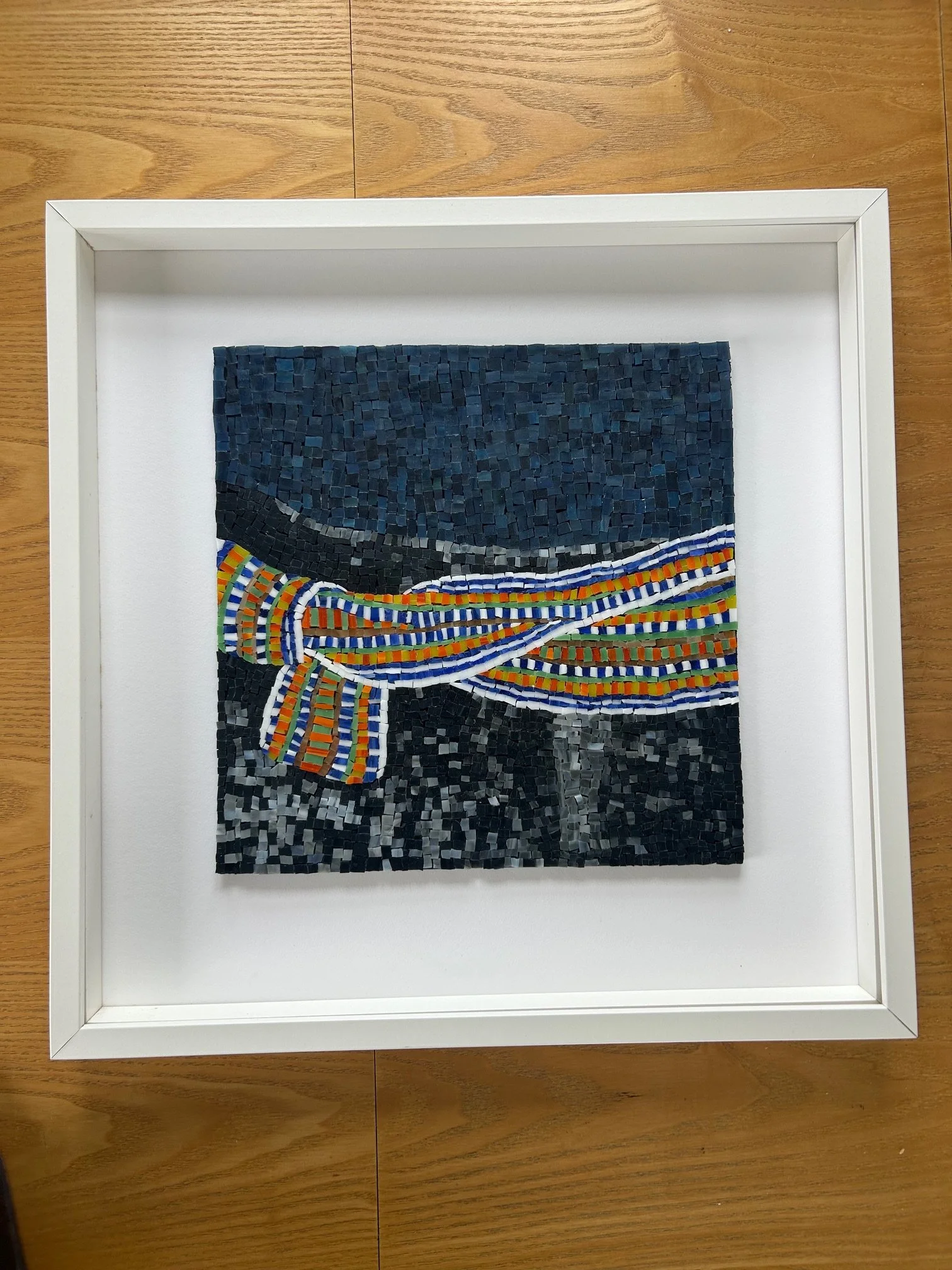 Mosaic art piece depicting the famous painting 'The Crios', a traditional hand-woven belt, enclosed in a white frame on a wooden surface.