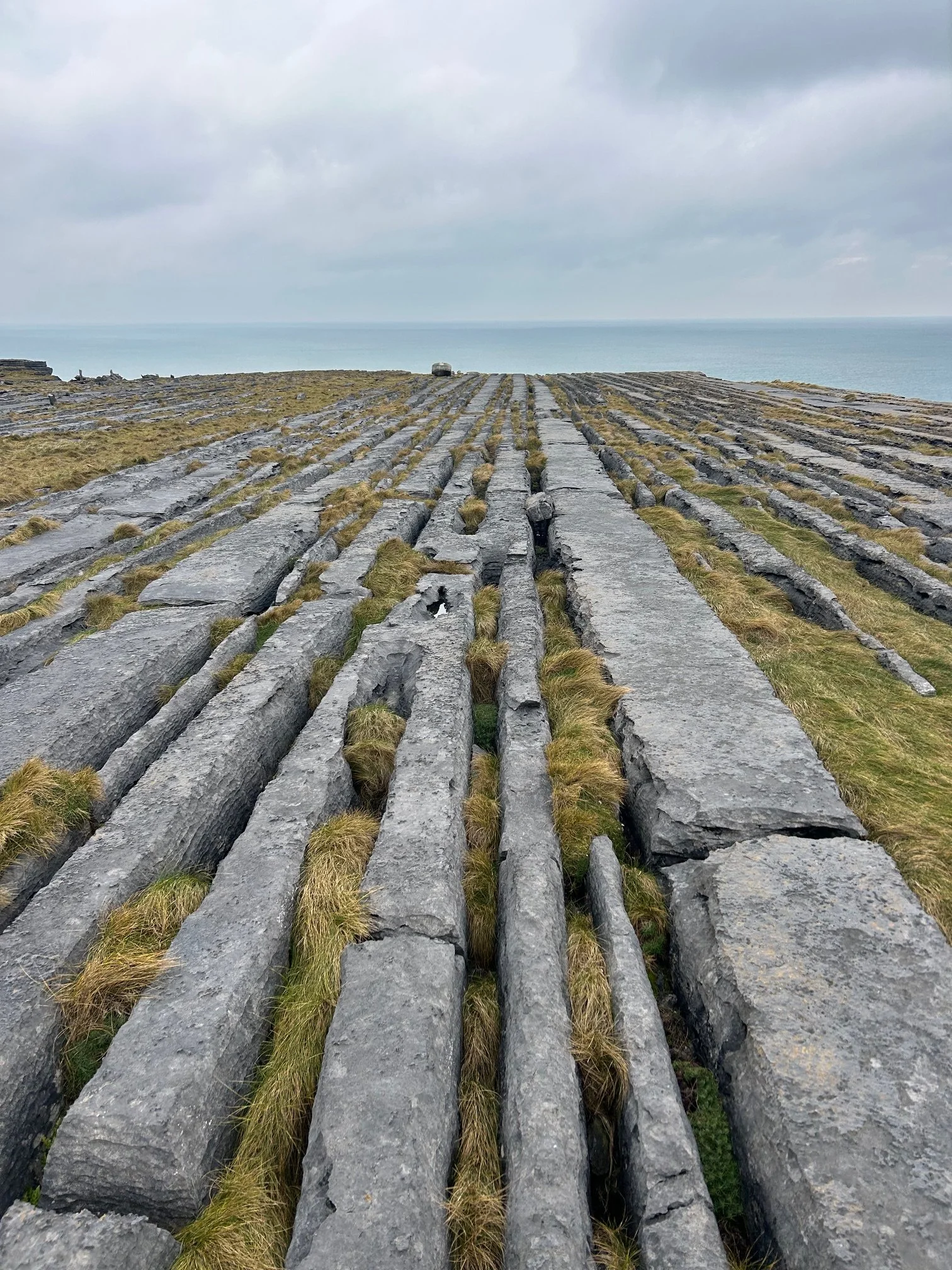 Stone pathway leading toward the horizon with water and cloudy sky in the background.