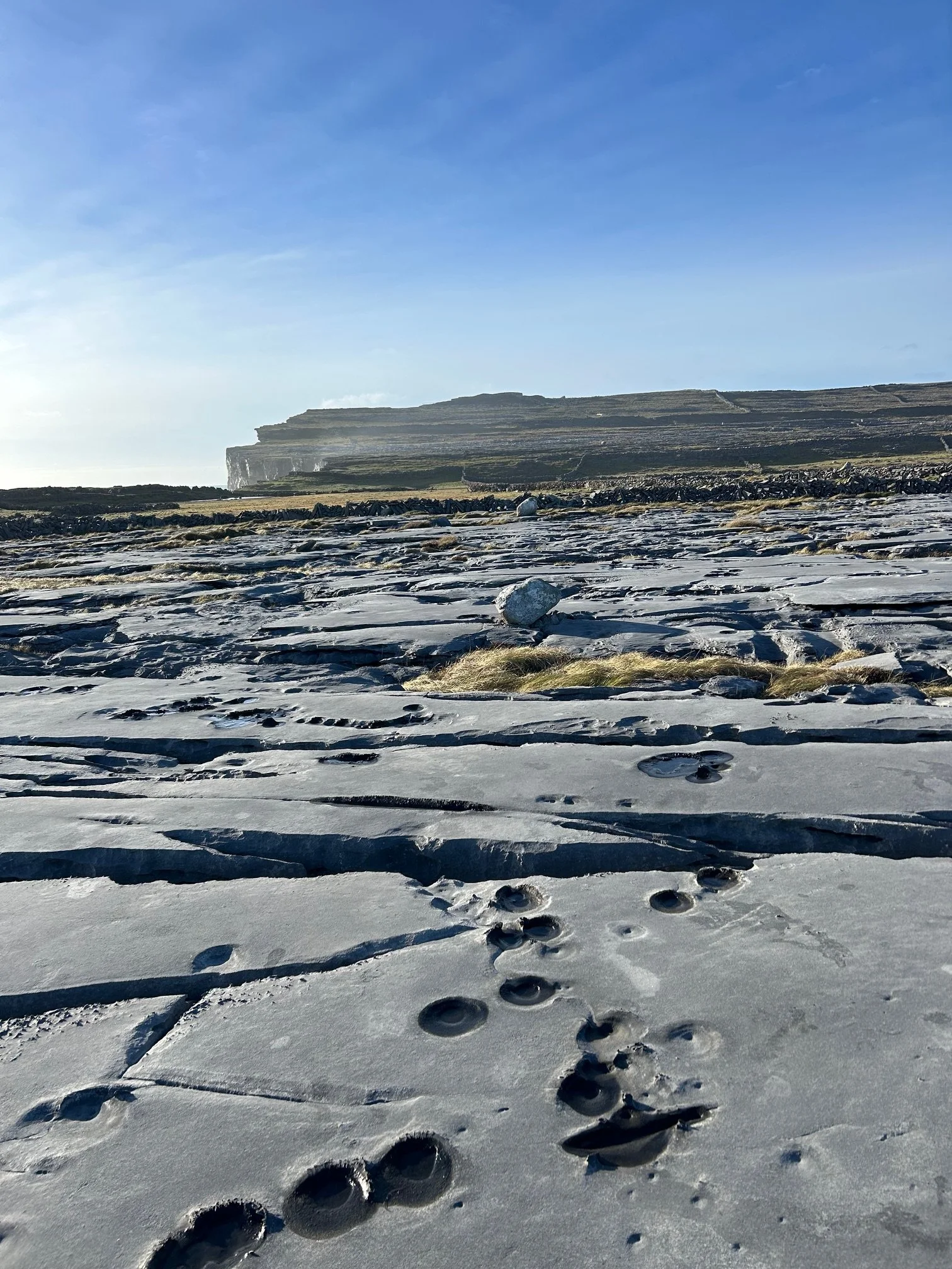 Footprints in snow leading towards distant cliffs under a blue sky.