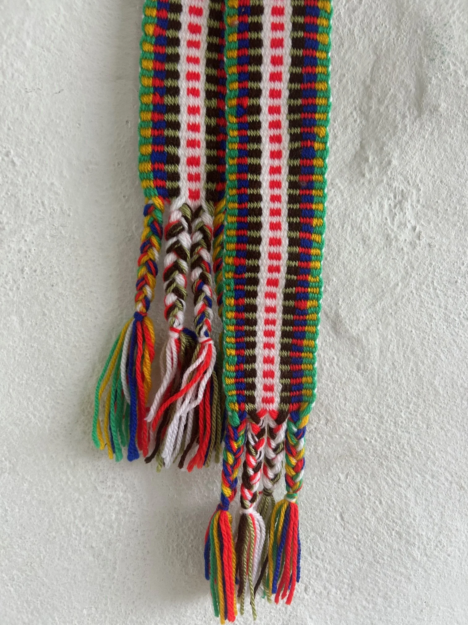 Colourful handwoven crios belt hanging against a white wall.