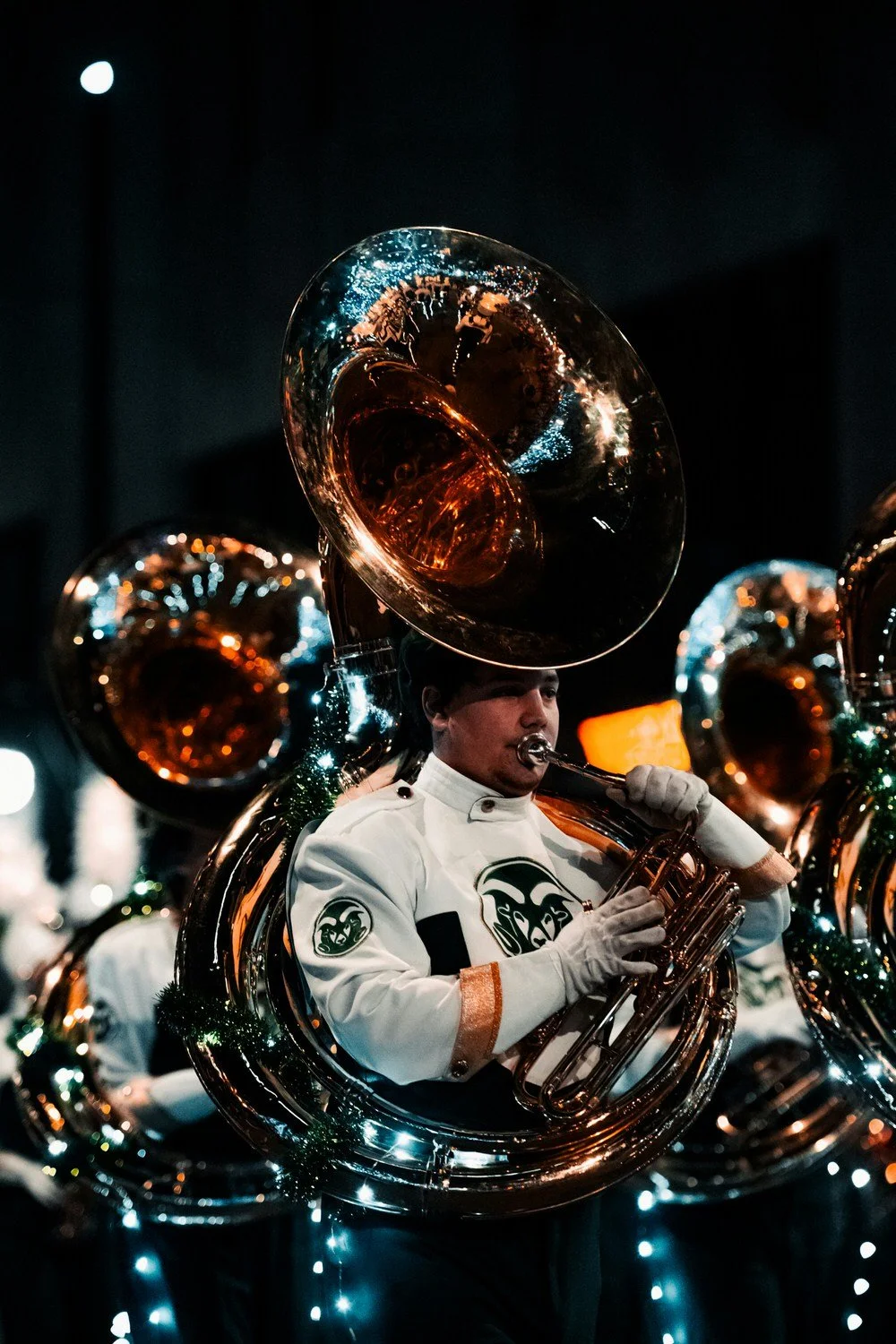 A musician playing a sousaphone during a nighttime parade or concert, decorated with Christmas lights.