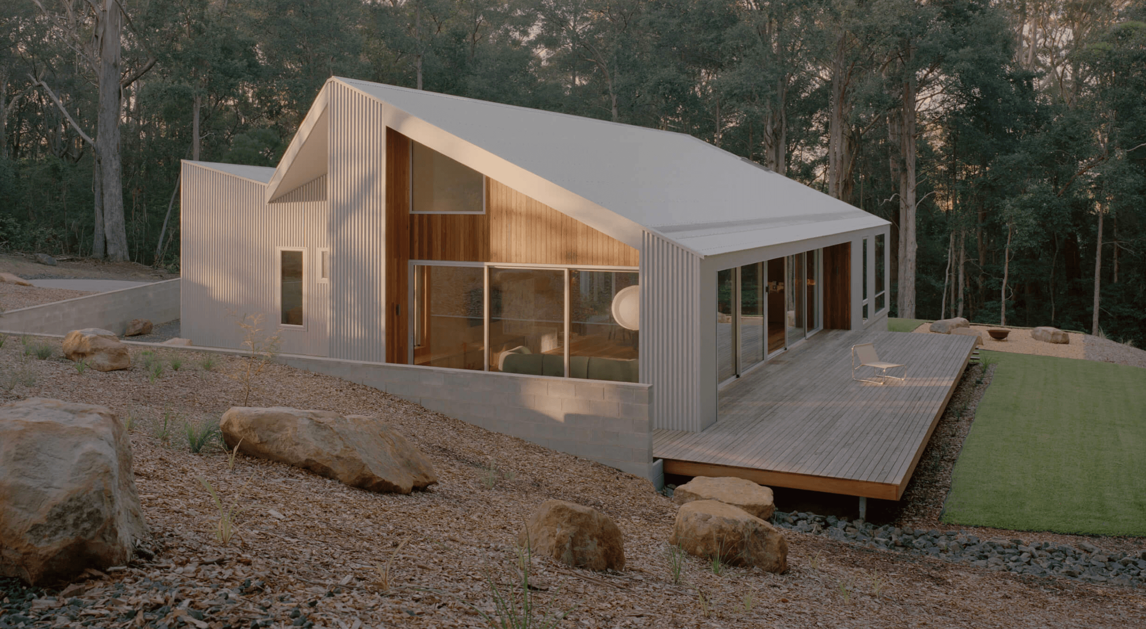 Ironbark House showcasing its white and wood exterior, large glass windows, and surrounding trees, set in the bushland canopy of country NSW.
