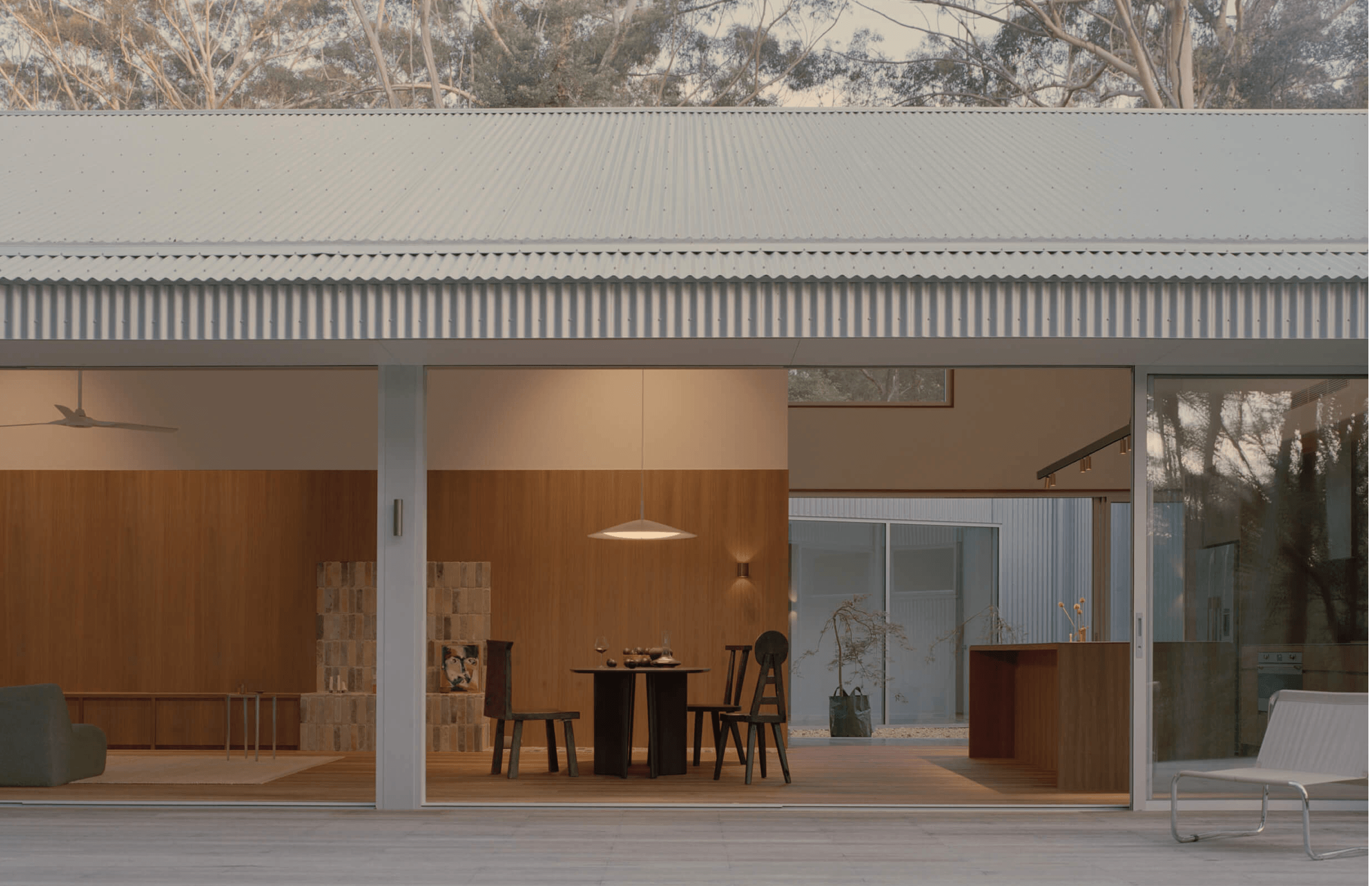 Ironbark House showcasing the open plan living quarters. Large glass sliding doors, timber wrapped interior, overlooking an outdoor seating area under the covered patio.
