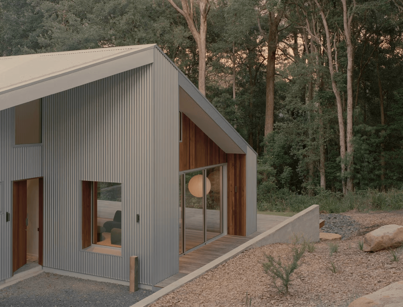 Ironbark House in the canopy showcasing metallic siding, large glass doors, and wooden accents, surrounded by a forest at dusk.