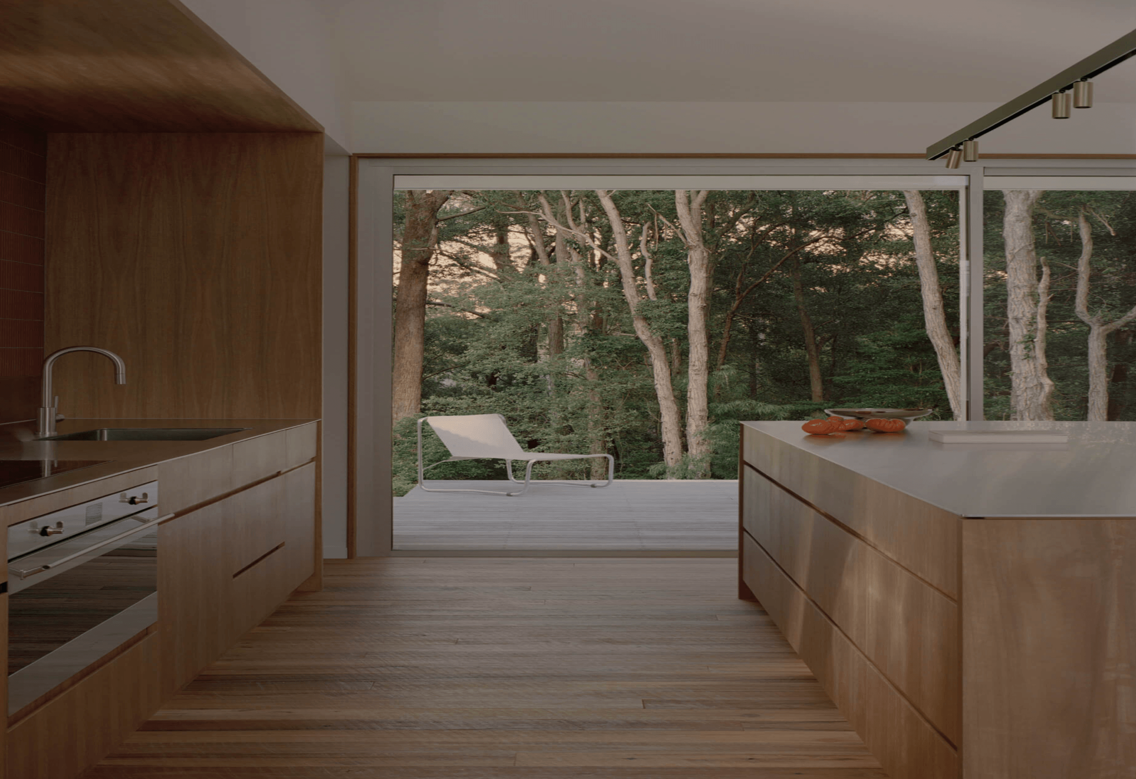 Interior view of Ironbark House kitchen with timber cabinets, a full-width sliding glass door leading to a deck, outdoor trees, and a lounge area.