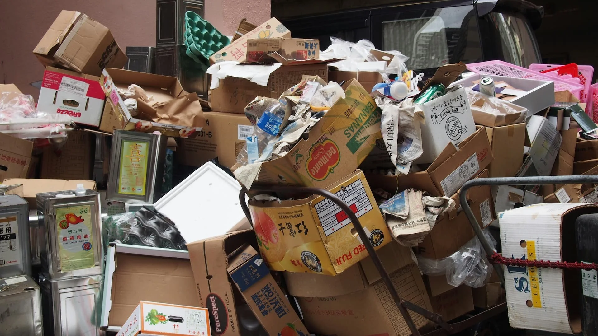 A large pile of mixed garbage including cardboard boxes, plastic bottles, and paper scraps, with some of the boxes labeled in Asian characters.