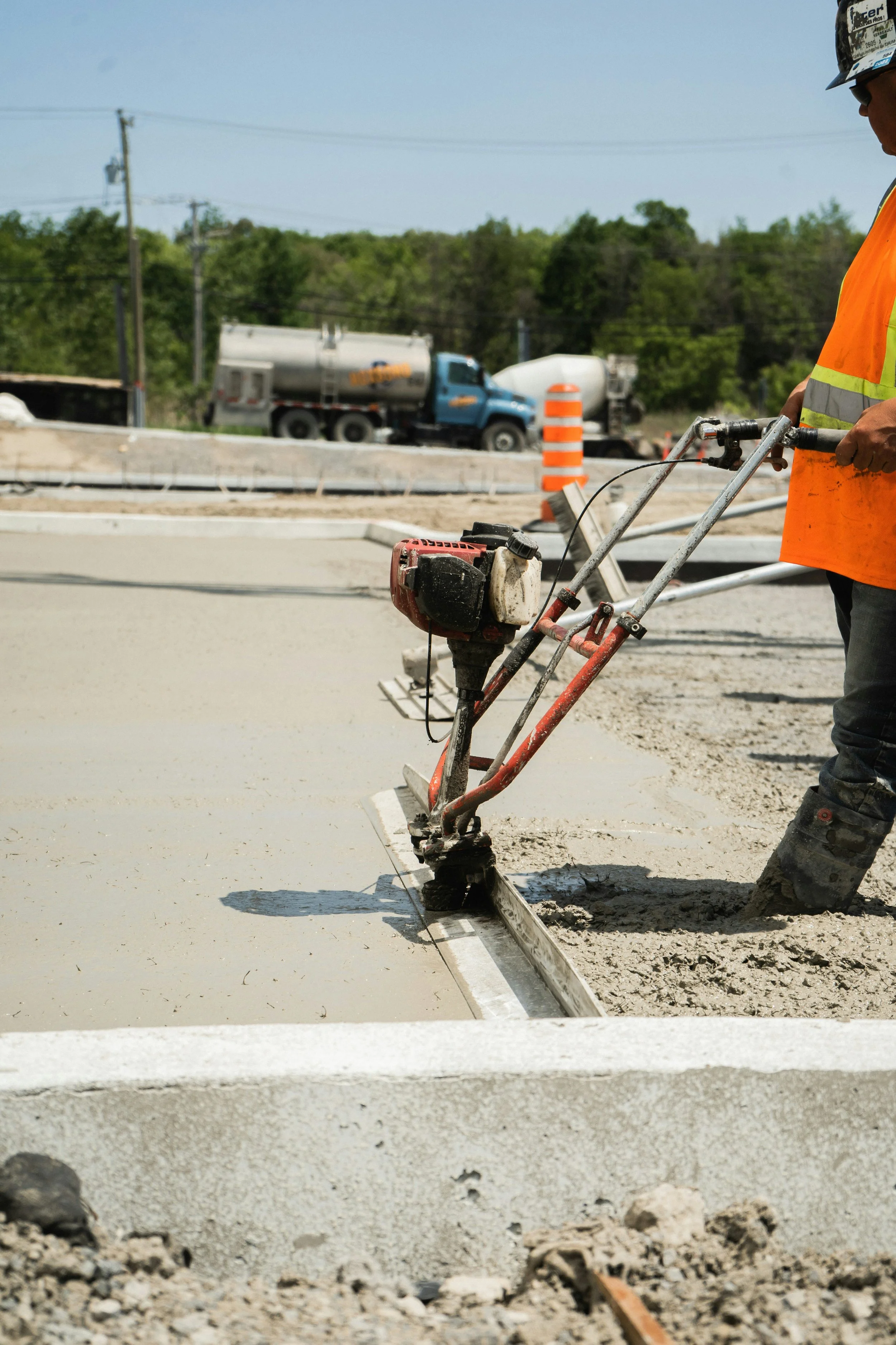A construction worker operating a power screed on freshly poured concrete at a construction site.