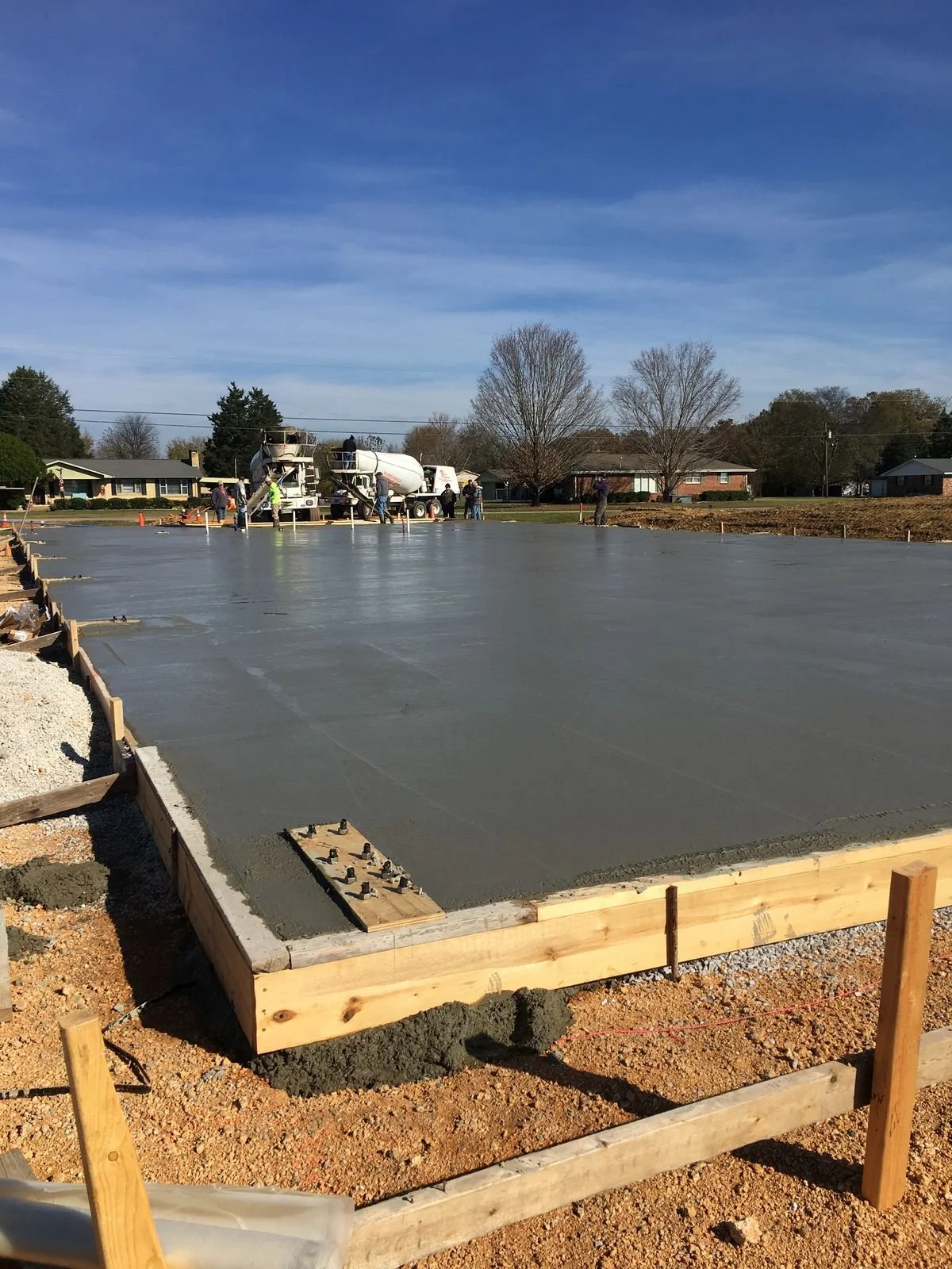 Construction workers pouring and leveling concrete on a building foundation in a suburban neighborhood.