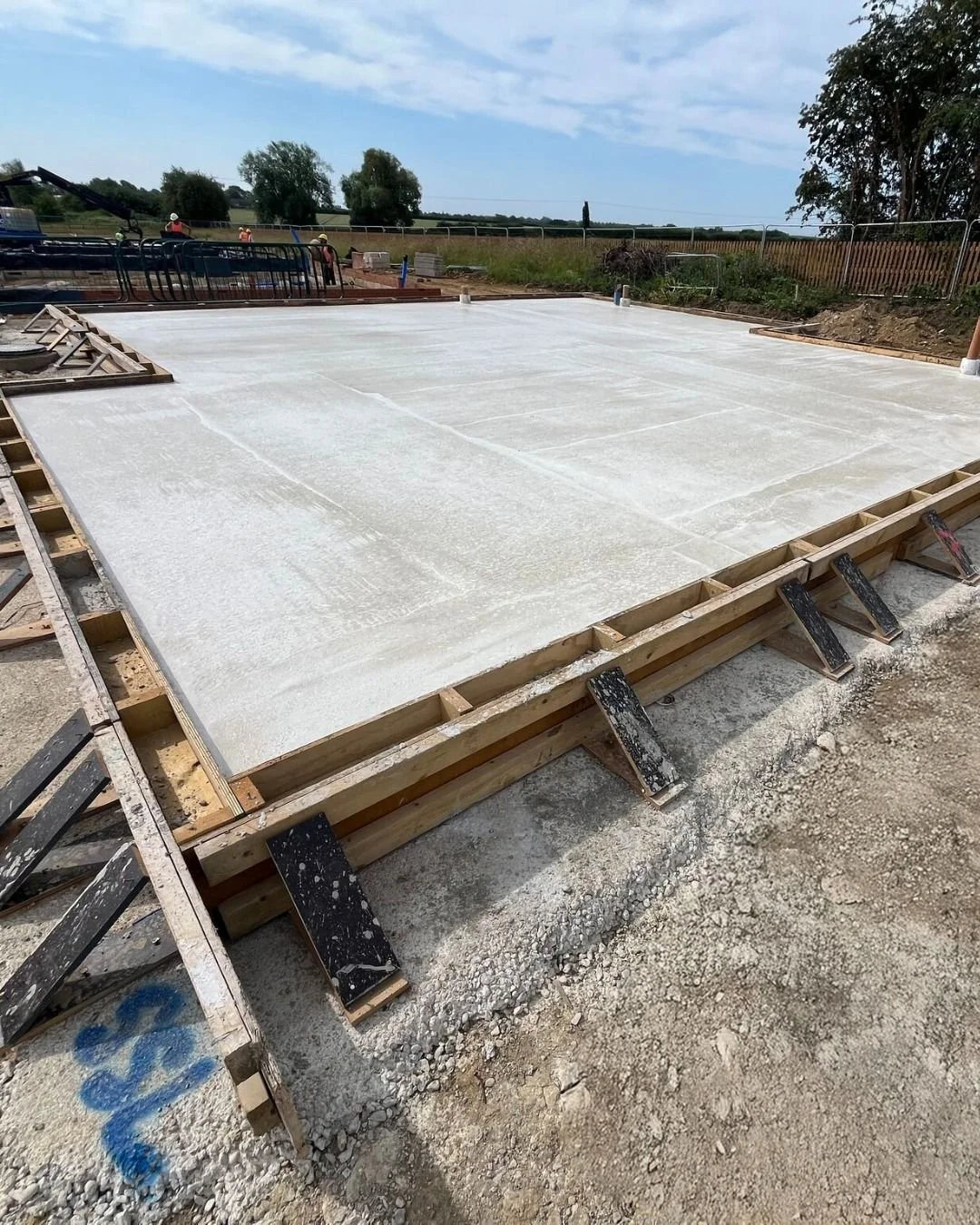 Concrete foundation being poured and leveled on a construction site with wooden forms and rebar in place.