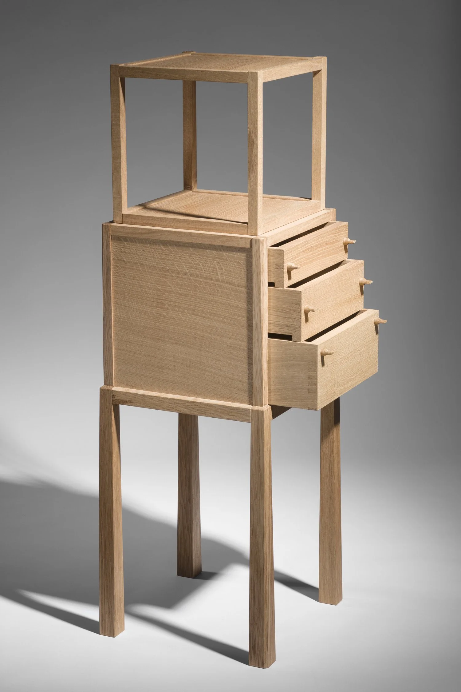 A wooden furniture piece with a four-legged stand, a closed cabinet with drawers, and an open display area on top.