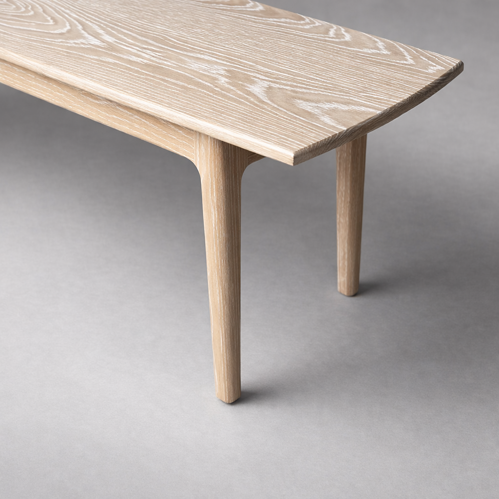 Close-up of a light-colored wooden table with angled legs against a gray background.