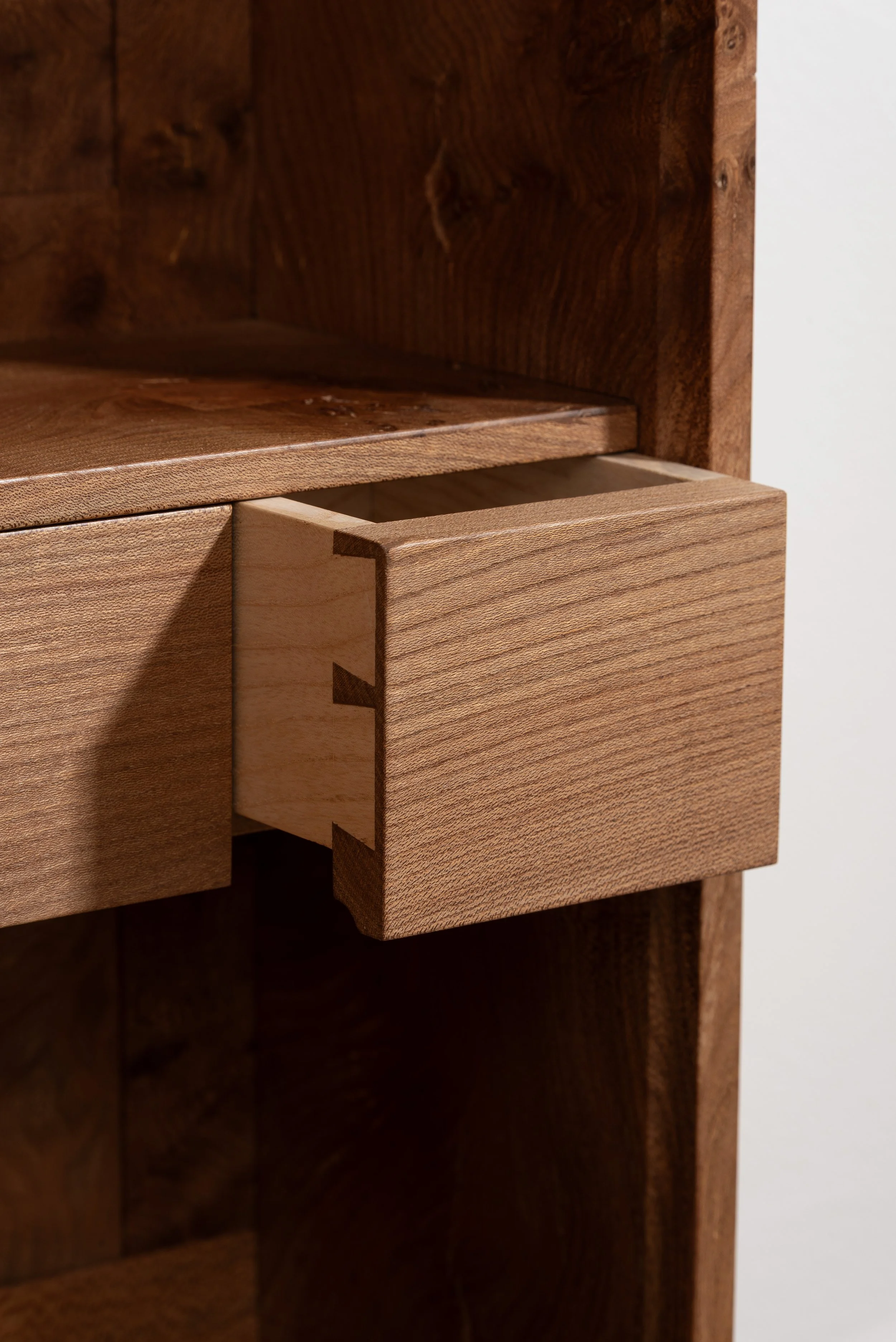 Close-up of a wooden drawer partially pulled out of a wooden furniture piece, showing dovetail joint construction.