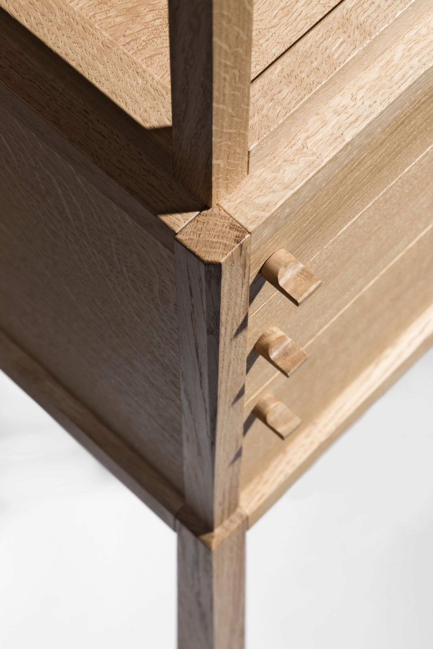 Close-up of a wooden furniture piece, showing a corner with a small vertical support and three small wooden knobs or pegs on the front side, made of light-colored wood.